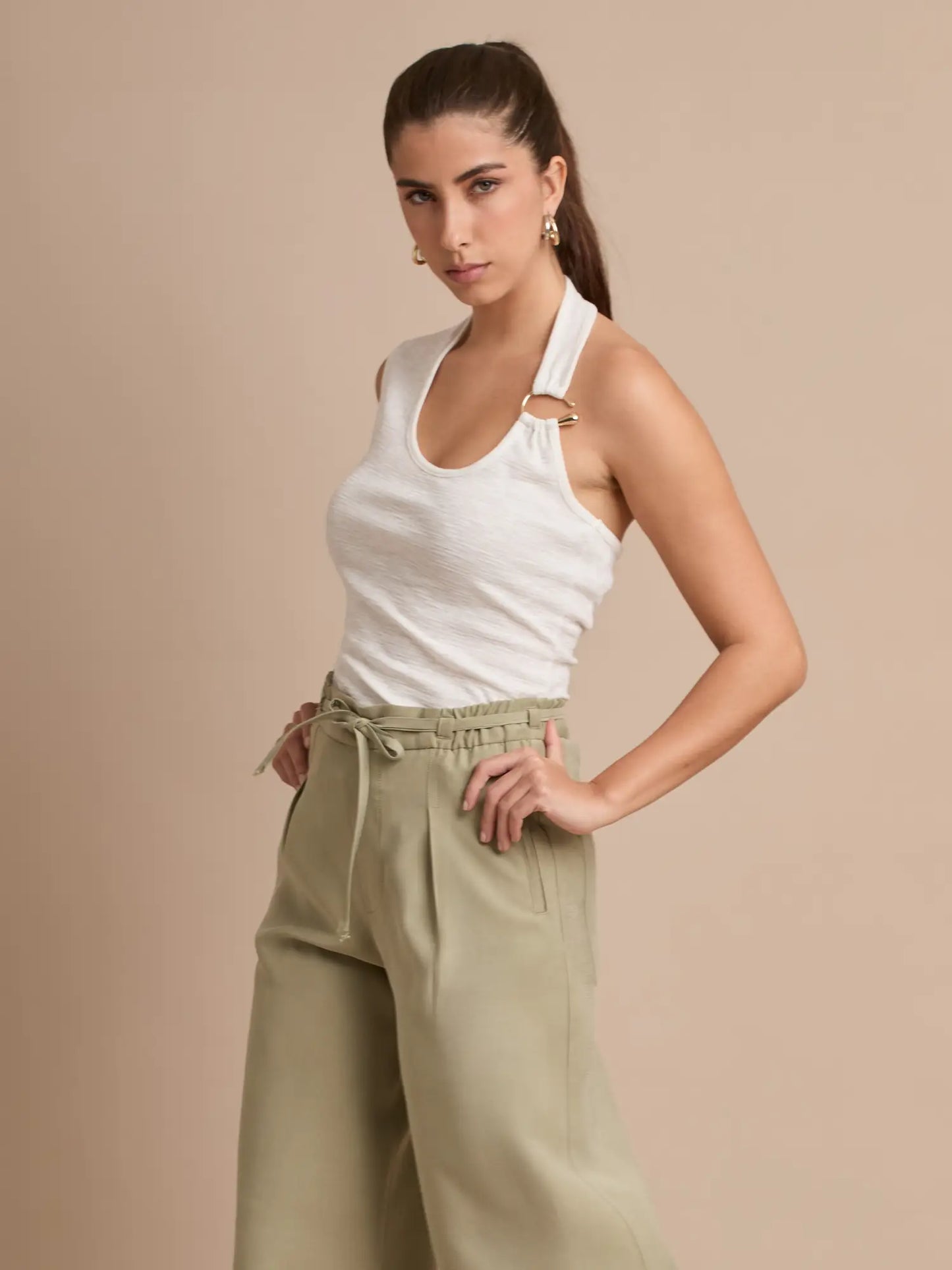 Eleva tu estilo con esta blusa halter en tono blanco puro, diseñada con un corte asimétrico y un aro dorado que añade un toque moderno y sofisticado. Perfecta para looks frescos y versátiles.