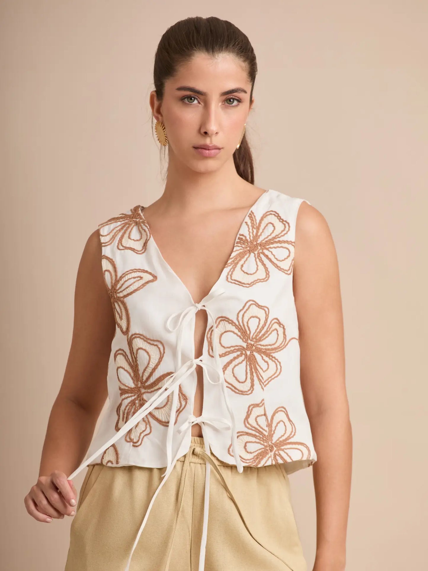 Este chaleco blanco ofrece un diseño ligero y moderno con bordado floral contrastante y amarre frontal. Perfecto para combinar con pantalones neutros o mezclilla.