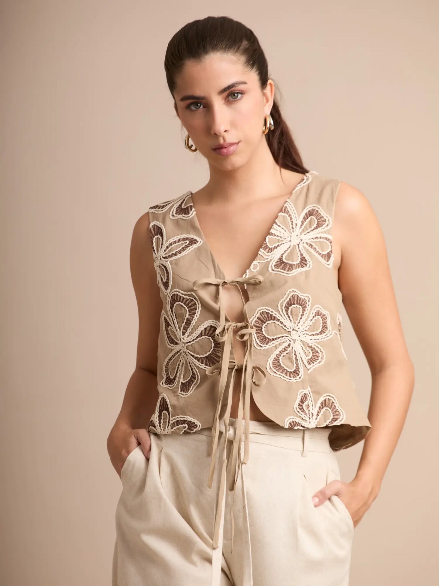 El chaleco Corfú camel destaca por sus bordados texturizados y un corte favorecedor sin mangas, ideal para darle un toque sofisticado y natural a tu outfit.