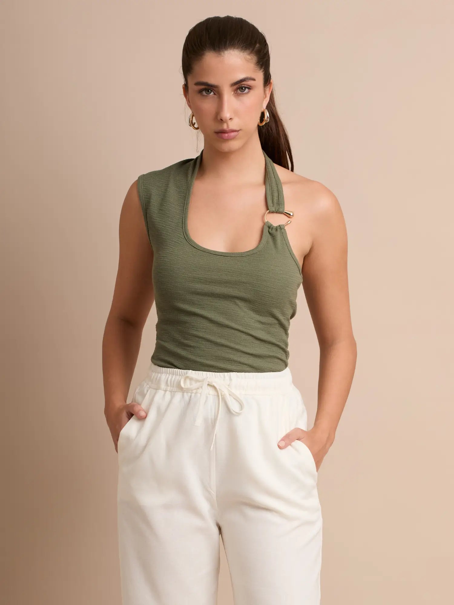 Ajustado y favorecedor, este top incorpora un delicado aro dorado que rompe la simetría del diseño halter. Un básico elevado para crear combinaciones versátiles durante el día o la noche.