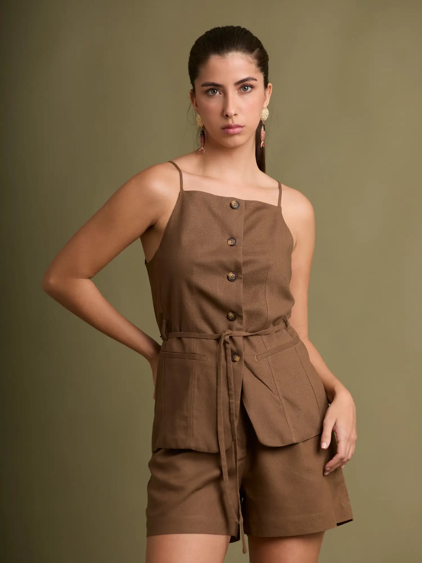 Este top café combina tirantes finos con amplios bolsillos frontales y botones al centro, creando una prenda fresca, versátil y perfecta para el día a día.
