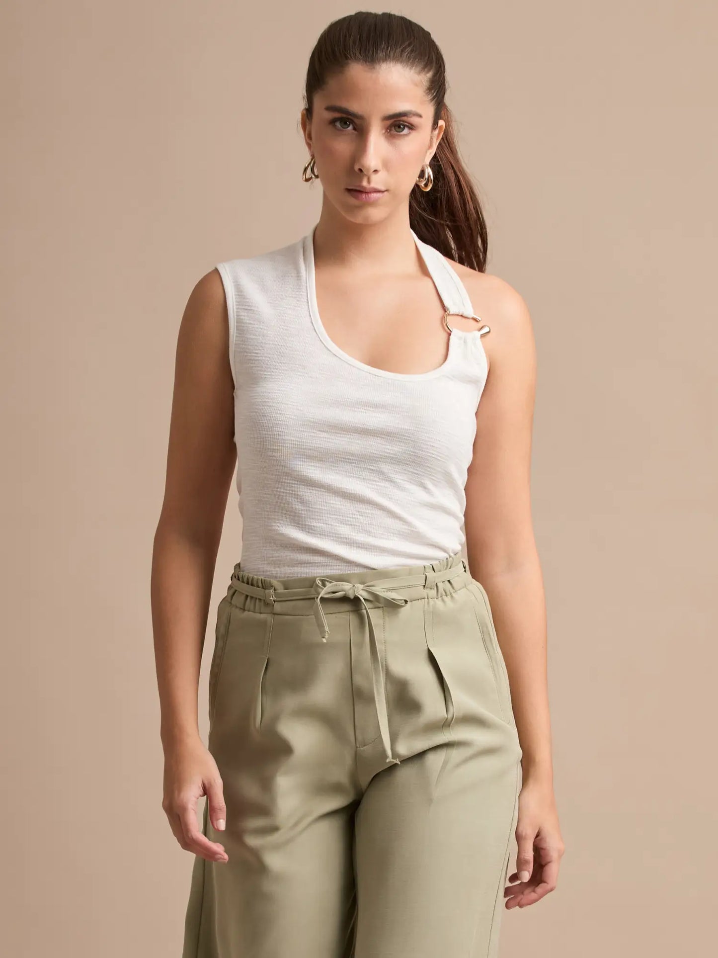 Luce un estilo limpio y sofisticado con este top blanco de corte halter asimétrico. Los aros dorados añaden un detalle único que resalta la parte superior del outfit.