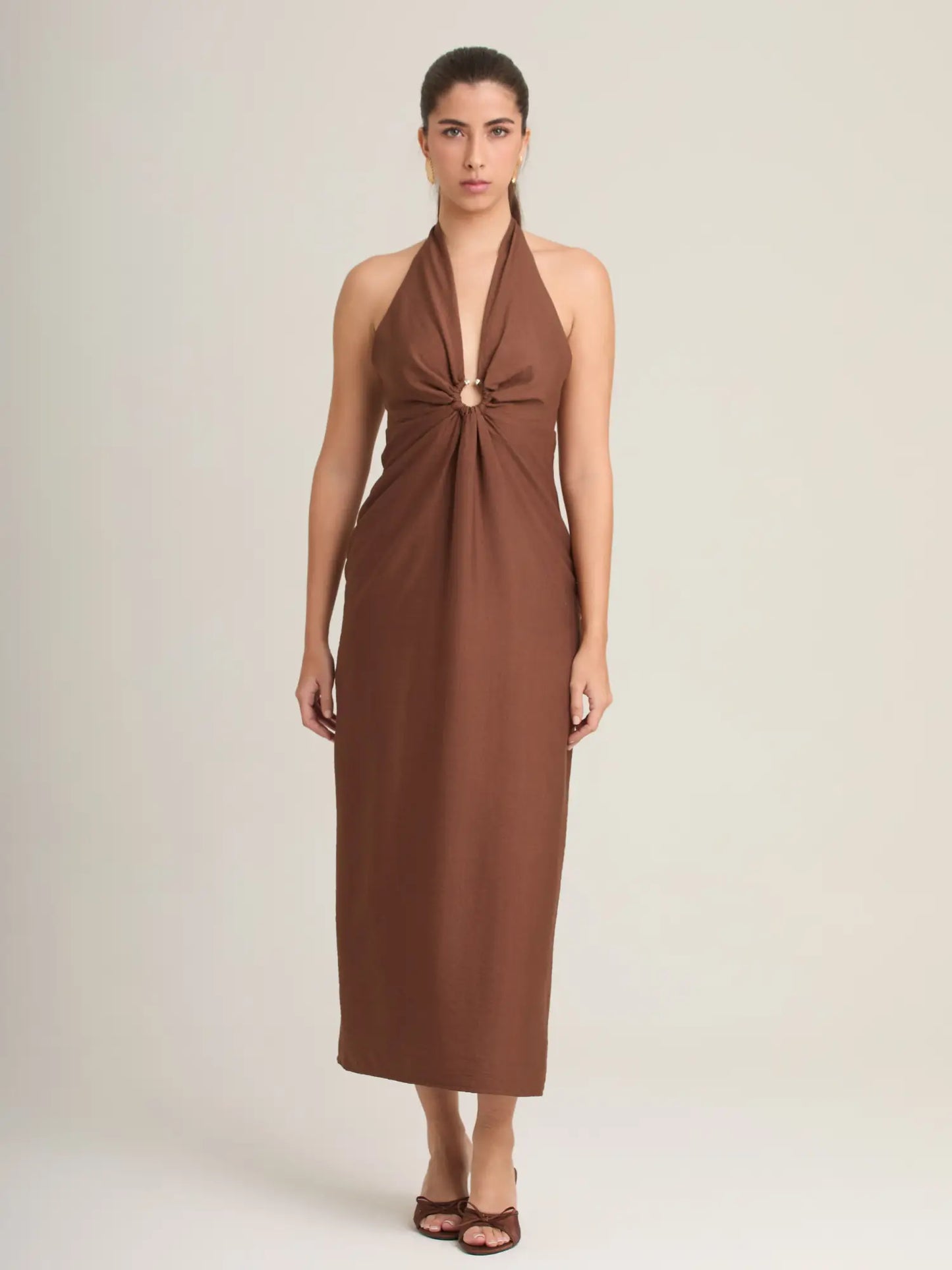 El vestido café midi destaca por su tejido fluido y su argolla metálica central que aporta dimensión al diseño. Una prenda moderna y versátil para eventos casuales o formales.