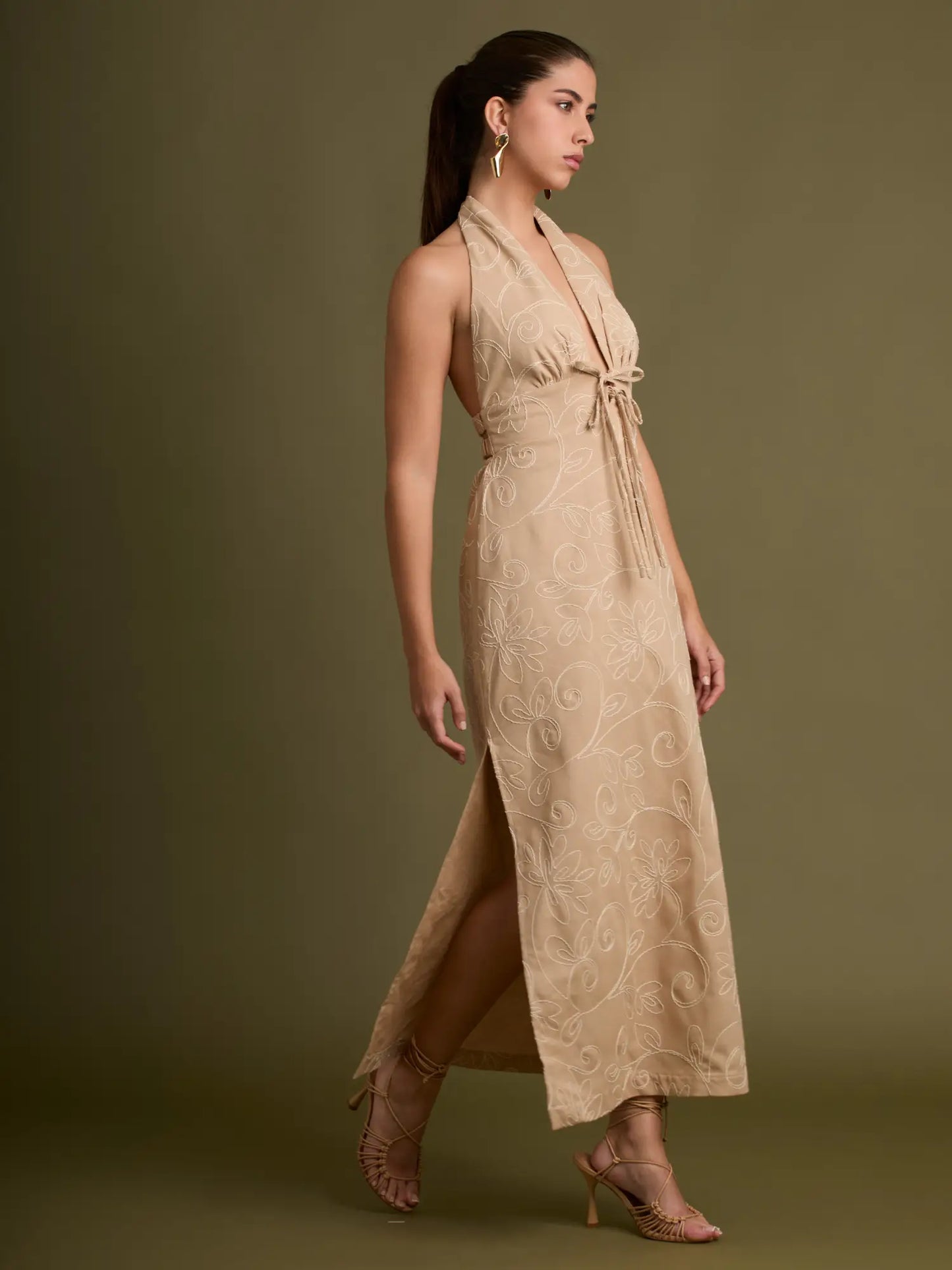 Un diseño sofisticado en tono beige con bordados florales en relieve, escote halter ajustable y una abertura lateral que aporta movimiento y feminidad a cada paso.