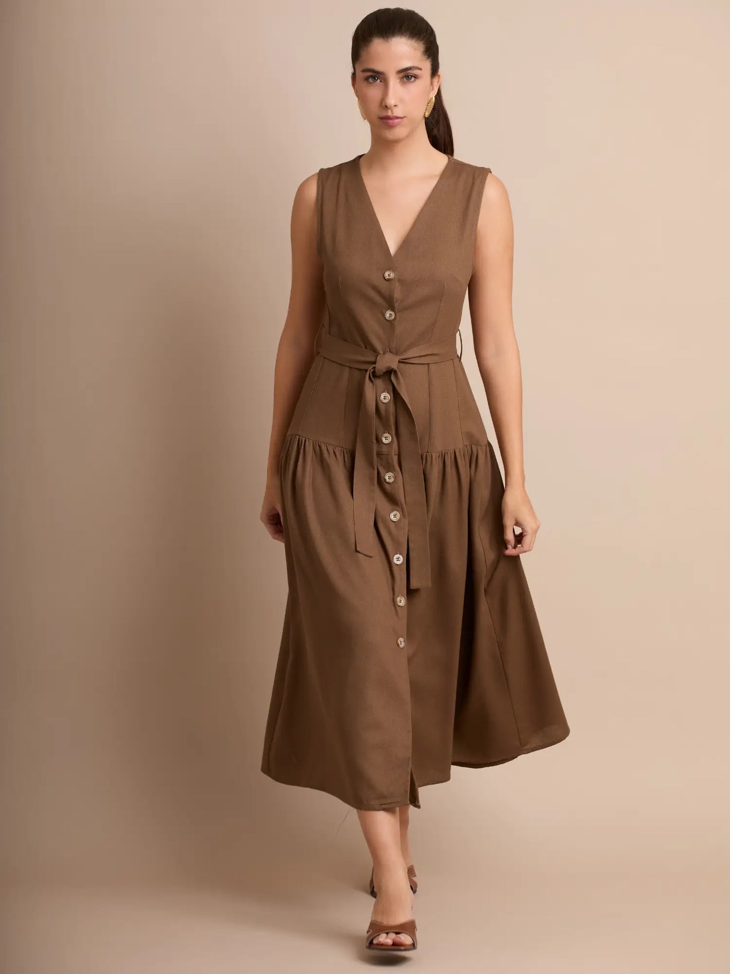 Este vestido midi en tono marrón presenta una botonadura frontal completa y un diseño elegante con caída suave. Su cinturón delgado ajusta la cintura para resaltar la silueta de manera natural.