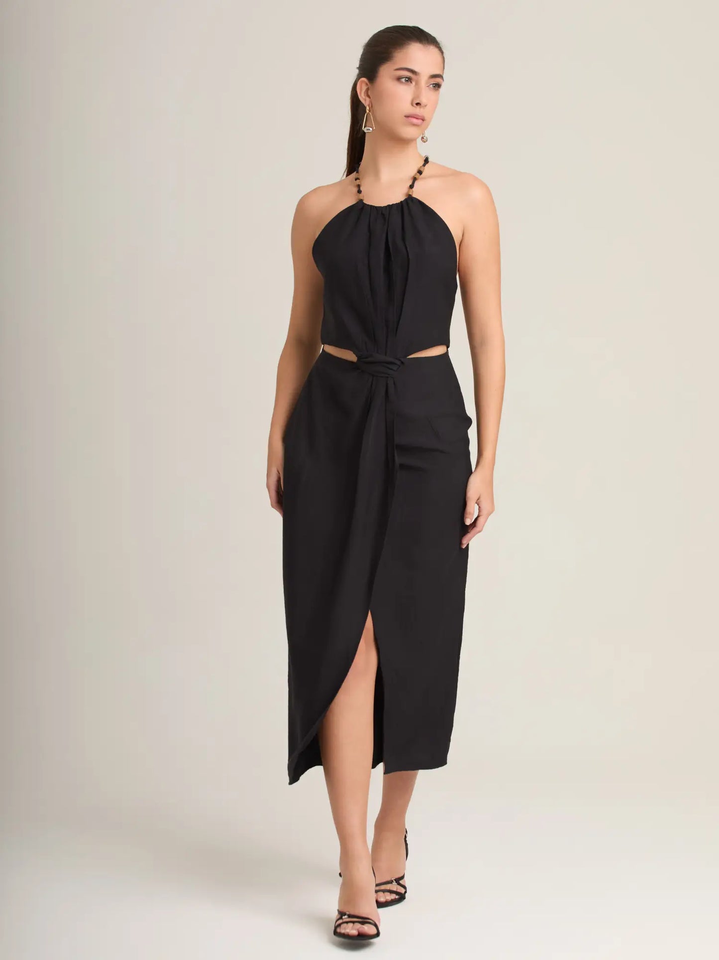 El vestido negro halter destaca por su diseño elegante con abertura lateral y falda cruzada que estiliza la figura. Su detalle cut-out en la cintura añade un toque moderno, perfecto para eventos nocturnos y ocasiones especiales.