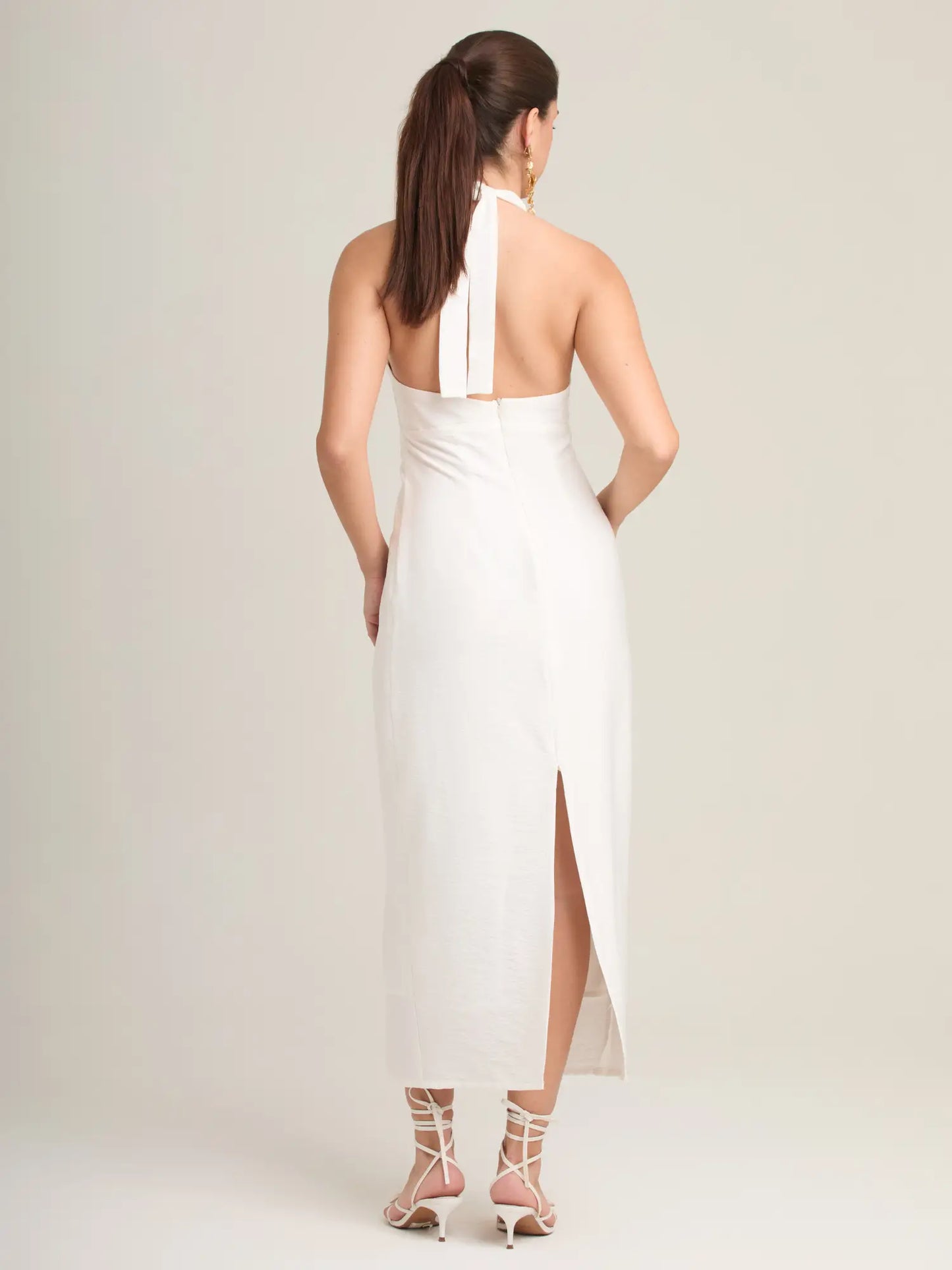 El vestido Palmeral Blanco destaca por su diseño sofisticado con escote halter profundo y un aro metálico frontal que realza la silueta. Su corte recto y minimalista lo convierte en una elección perfecta para eventos elegantes, cenas de verano o celebraciones al aire libre