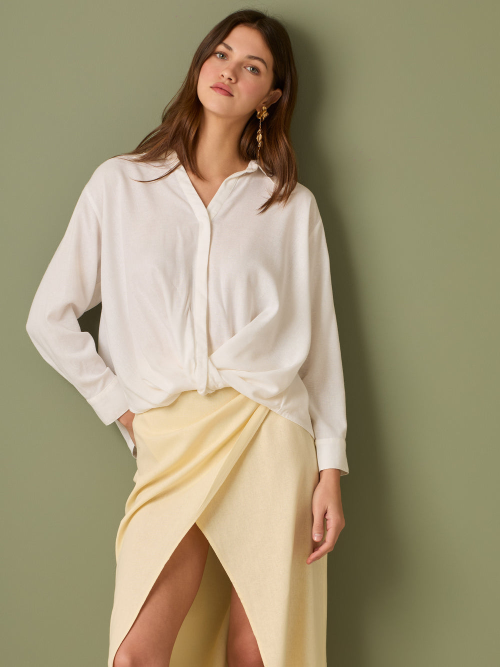 Esta blusa de manga larga tiene un estilo sofisticado y moderno. Presenta cuello clásico tipo camisero y un diseño de escote en "V" sutil que alarga visualmente el cuello. El detalle más destacado es el nudo frontal retorcido en la parte baja, que genera un efecto drapeado y asimétrico, aportando dinamismo y elegancia a la prenda. Los puños son anchos y estructurados, lo que refuerza el acabado pulido del diseño. Ideal para looks formales o smart-casual, combinada con pantalones de tiro alto o faldas.