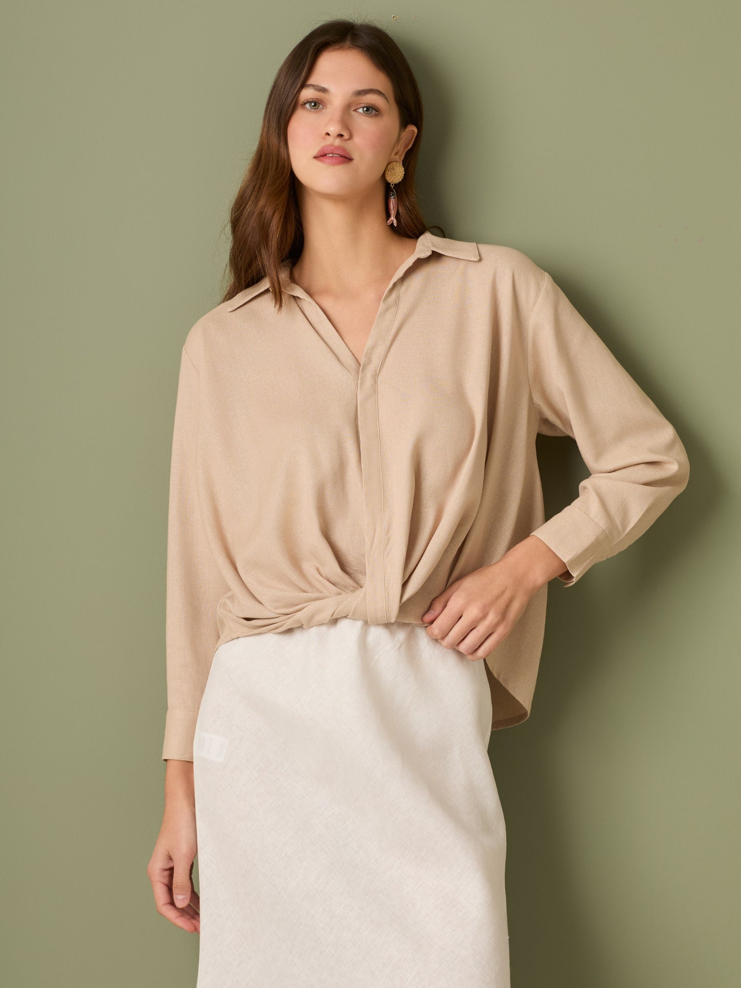 Esta blusa de manga larga tiene un estilo sofisticado y moderno. Presenta cuello clásico tipo camisero y un diseño de escote en "V" sutil que alarga visualmente el cuello. El detalle más destacado es el nudo frontal retorcido en la parte baja, que genera un efecto drapeado y asimétrico, aportando dinamismo y elegancia a la prenda. Los puños son anchos y estructurados, lo que refuerza el acabado pulido del diseño. Ideal para looks formales o smart-casual, combinada con pantalones de tiro alto o faldas.