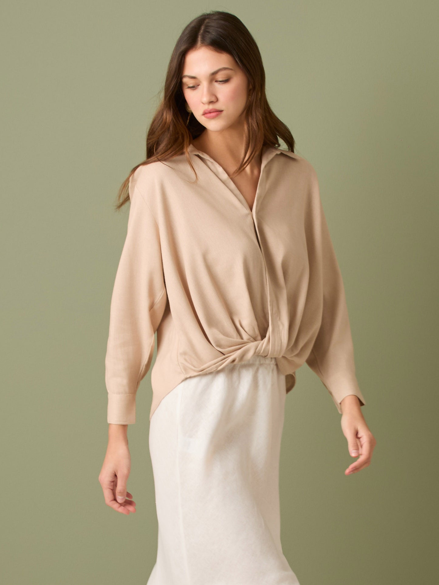 Esta blusa de manga larga tiene un estilo sofisticado y moderno. Presenta cuello clásico tipo camisero y un diseño de escote en "V" sutil que alarga visualmente el cuello. El detalle más destacado es el nudo frontal retorcido en la parte baja, que genera un efecto drapeado y asimétrico, aportando dinamismo y elegancia a la prenda. Los puños son anchos y estructurados, lo que refuerza el acabado pulido del diseño. Ideal para looks formales o smart-casual, combinada con pantalones de tiro alto o faldas.