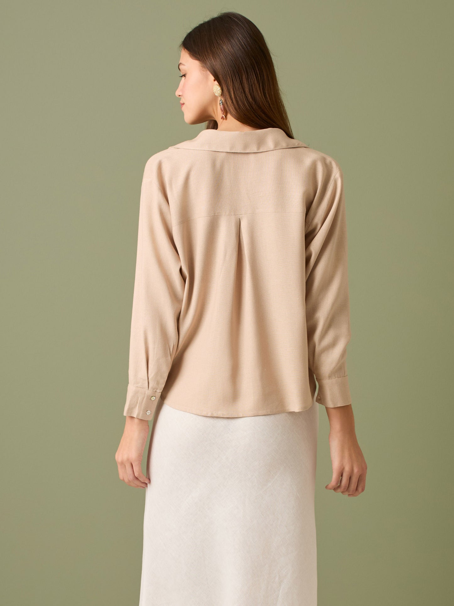 Esta blusa de manga larga tiene un estilo sofisticado y moderno. Presenta cuello clásico tipo camisero y un diseño de escote en "V" sutil que alarga visualmente el cuello. El detalle más destacado es el nudo frontal retorcido en la parte baja, que genera un efecto drapeado y asimétrico, aportando dinamismo y elegancia a la prenda. Los puños son anchos y estructurados, lo que refuerza el acabado pulido del diseño. Ideal para looks formales o smart-casual, combinada con pantalones de tiro alto o faldas.