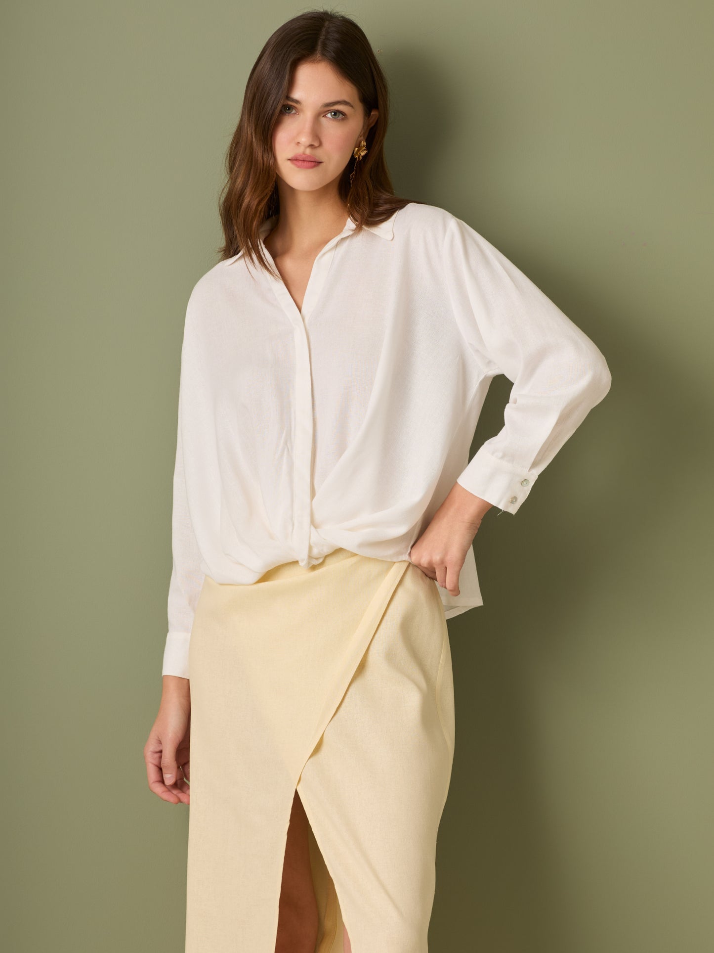 Esta blusa de manga larga tiene un estilo sofisticado y moderno. Presenta cuello clásico tipo camisero y un diseño de escote en "V" sutil que alarga visualmente el cuello. El detalle más destacado es el nudo frontal retorcido en la parte baja, que genera un efecto drapeado y asimétrico, aportando dinamismo y elegancia a la prenda. Los puños son anchos y estructurados, lo que refuerza el acabado pulido del diseño. Ideal para looks formales o smart-casual, combinada con pantalones de tiro alto o faldas.