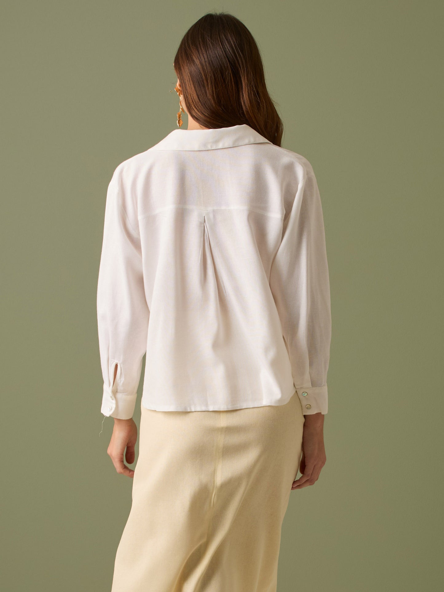 Esta blusa de manga larga tiene un estilo sofisticado y moderno. Presenta cuello clásico tipo camisero y un diseño de escote en "V" sutil que alarga visualmente el cuello. El detalle más destacado es el nudo frontal retorcido en la parte baja, que genera un efecto drapeado y asimétrico, aportando dinamismo y elegancia a la prenda. Los puños son anchos y estructurados, lo que refuerza el acabado pulido del diseño. Ideal para looks formales o smart-casual, combinada con pantalones de tiro alto o faldas.