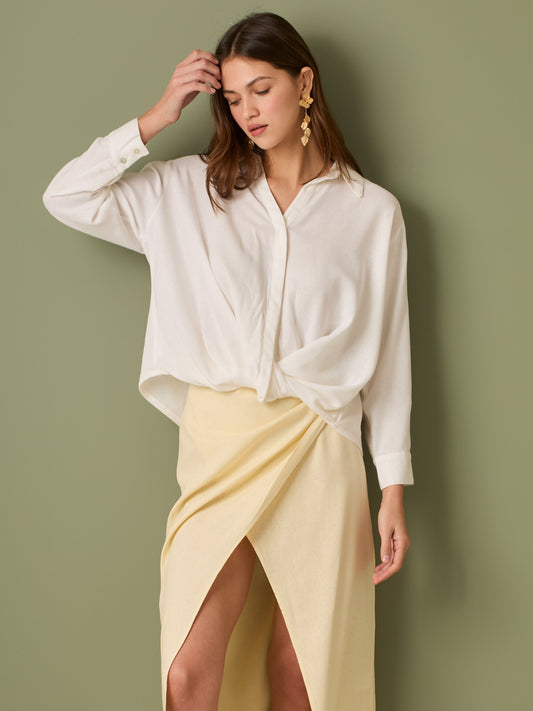 Esta blusa de manga larga tiene un estilo sofisticado y moderno. Presenta cuello clásico tipo camisero y un diseño de escote en "V" sutil que alarga visualmente el cuello. El detalle más destacado es el nudo frontal retorcido en la parte baja, que genera un efecto drapeado y asimétrico, aportando dinamismo y elegancia a la prenda. Los puños son anchos y estructurados, lo que refuerza el acabado pulido del diseño. Ideal para looks formales o smart-casual, combinada con pantalones de tiro alto o faldas.