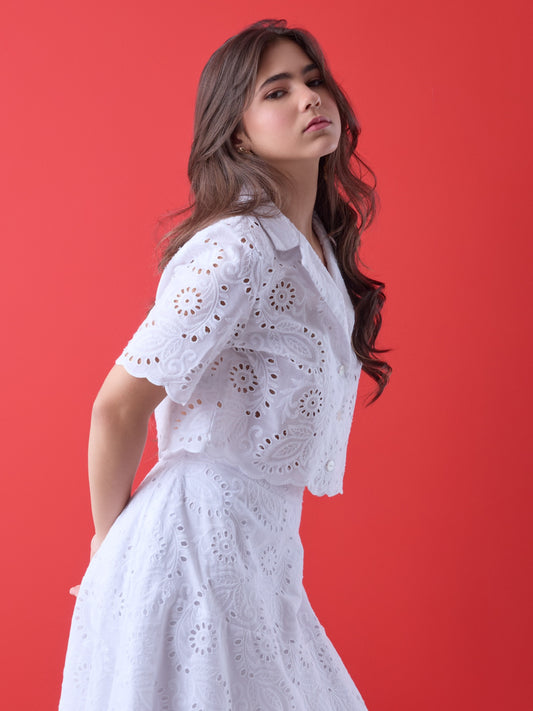 Con un diseño delicado y femenino, esta blusa corta presenta bordado calado en todo su contorno, aportando textura y un aire artesanal. El cuello camisero, la silueta relajada y las mangas cortas estructuradas la convierten en una prenda ideal para looks frescos y elegantes. Perfecta para combinar con faldas de talle alto o pantalones sutiles en ocasiones de día con un estilo impecable.