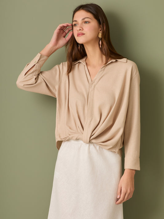 Esta blusa de manga larga tiene un estilo sofisticado y moderno. Presenta cuello clásico tipo camisero y un diseño de escote en "V" sutil que alarga visualmente el cuello. El detalle más destacado es el nudo frontal retorcido en la parte baja, que genera un efecto drapeado y asimétrico, aportando dinamismo y elegancia a la prenda. Los puños son anchos y estructurados, lo que refuerza el acabado pulido del diseño. Ideal para looks formales o smart-casual, combinada con pantalones de tiro alto o faldas.