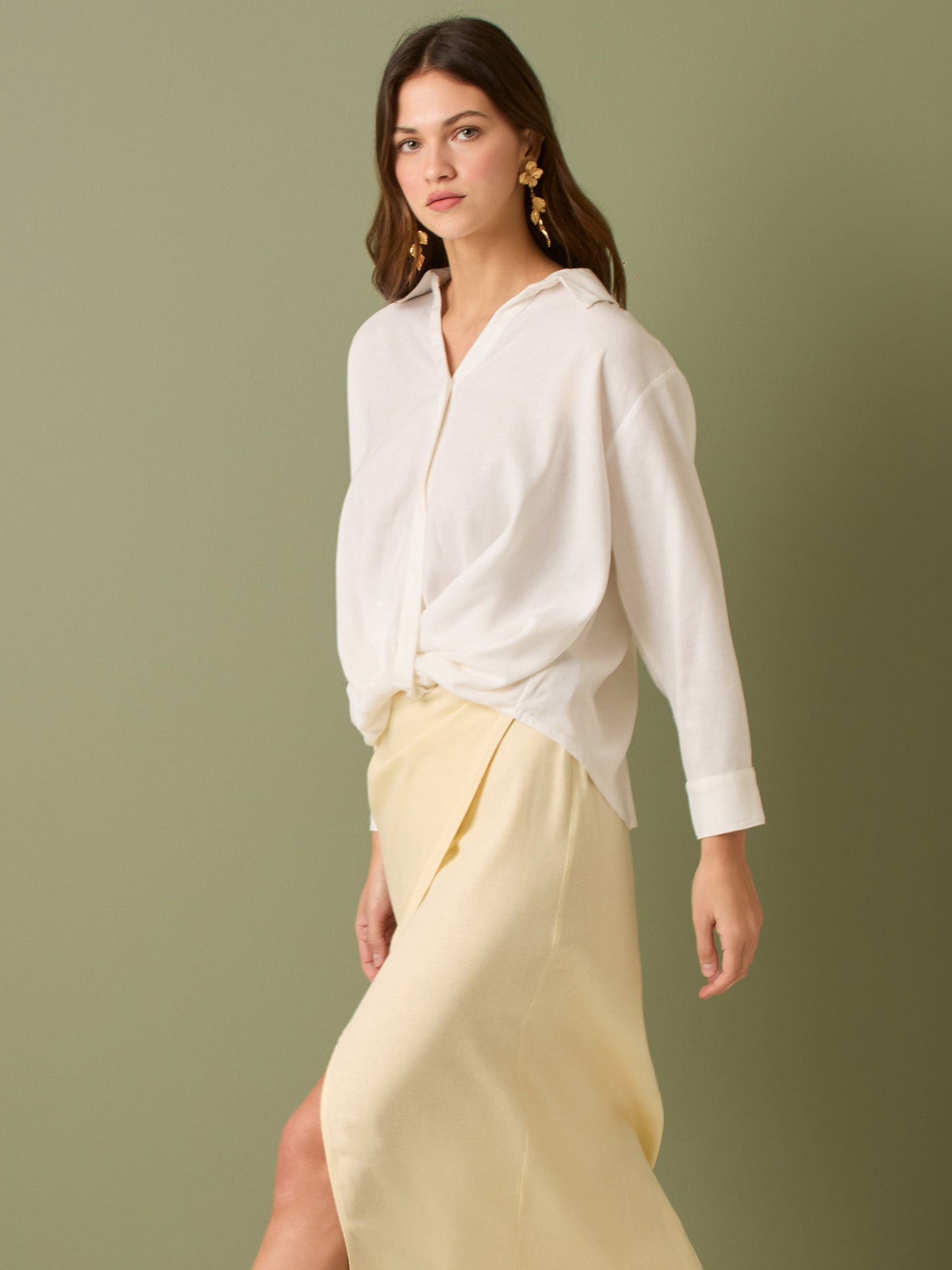 Esta blusa de manga larga tiene un estilo sofisticado y moderno. Presenta cuello clásico tipo camisero y un diseño de escote en "V" sutil que alarga visualmente el cuello. El detalle más destacado es el nudo frontal retorcido en la parte baja, que genera un efecto drapeado y asimétrico, aportando dinamismo y elegancia a la prenda. Los puños son anchos y estructurados, lo que refuerza el acabado pulido del diseño. Ideal para looks formales o smart-casual, combinada con pantalones de tiro alto o faldas.