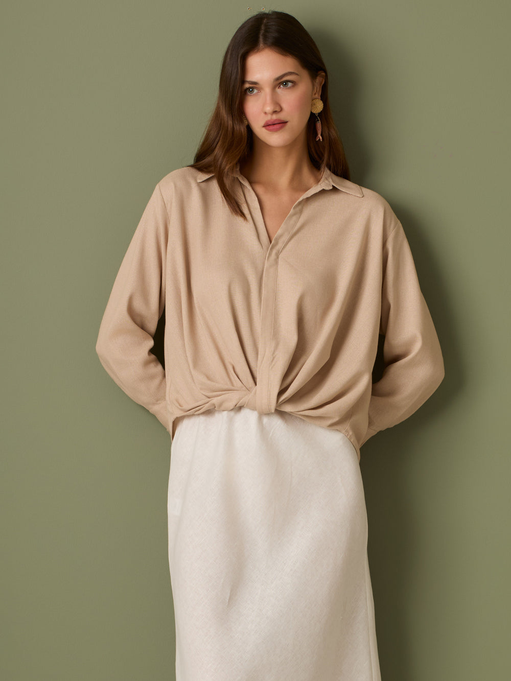 Esta blusa de manga larga tiene un estilo sofisticado y moderno. Presenta cuello clásico tipo camisero y un diseño de escote en "V" sutil que alarga visualmente el cuello. El detalle más destacado es el nudo frontal retorcido en la parte baja, que genera un efecto drapeado y asimétrico, aportando dinamismo y elegancia a la prenda. Los puños son anchos y estructurados, lo que refuerza el acabado pulido del diseño. Ideal para looks formales o smart-casual, combinada con pantalones de tiro alto o faldas.