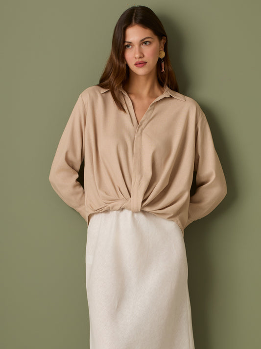 Esta blusa de manga larga tiene un estilo sofisticado y moderno. Presenta cuello clásico tipo camisero y un diseño de escote en "V" sutil que alarga visualmente el cuello. El detalle más destacado es el nudo frontal retorcido en la parte baja, que genera un efecto drapeado y asimétrico, aportando dinamismo y elegancia a la prenda. Los puños son anchos y estructurados, lo que refuerza el acabado pulido del diseño. Ideal para looks formales o smart-casual, combinada con pantalones de tiro alto o faldas.