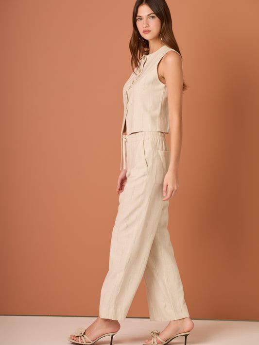 Blusa sin mangas de corte limpio y femenino. Cuello redondo y botonadura frontal con botones tipo joya; pinzas que definen el torso y bajo ligeramente curvado con pequeña abertura al centro. El sutil rayado vertical estiliza la figura. Ideal para combinar con el pantalón a juego o faldas altas para un look pulido.