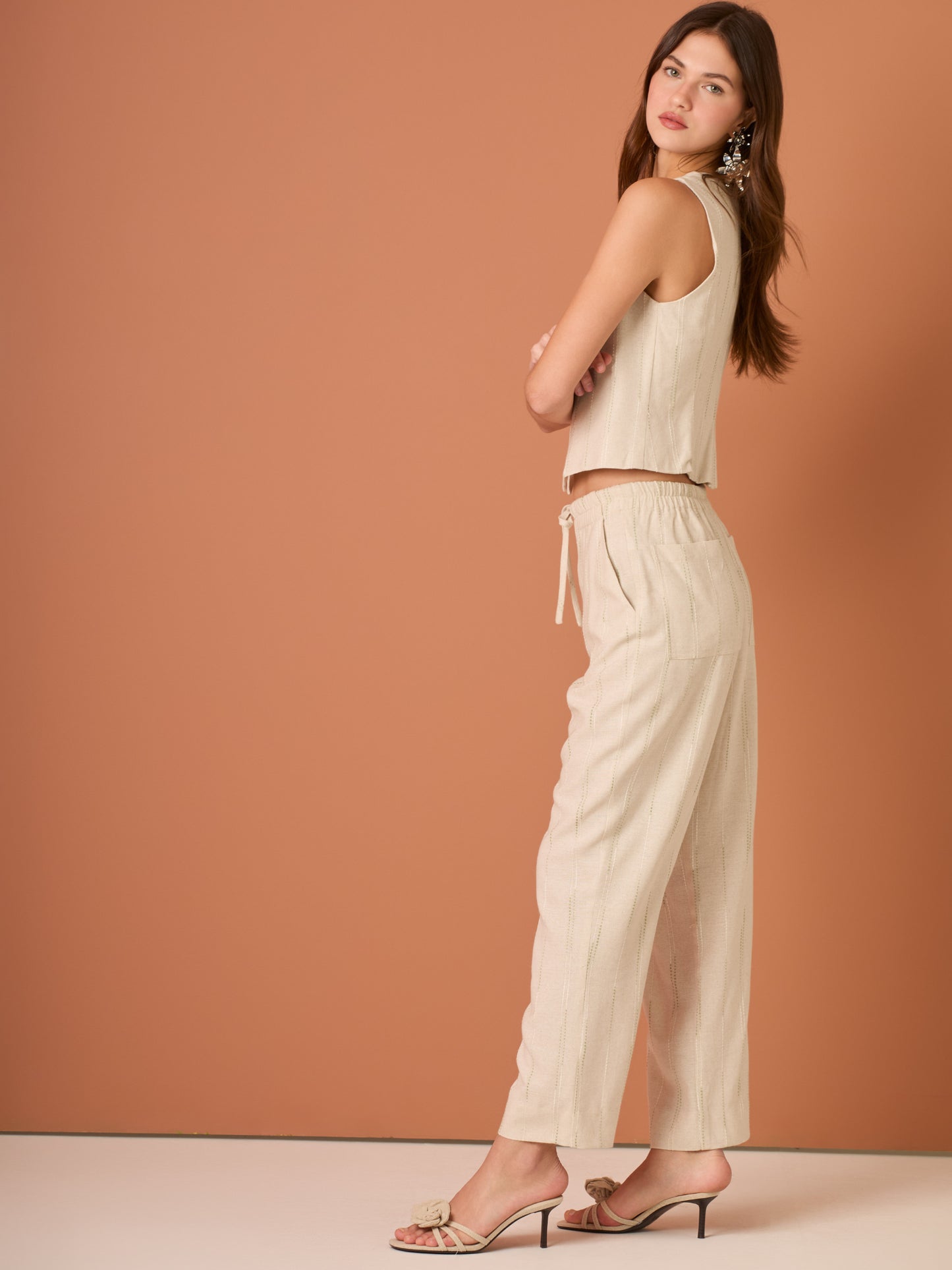 Blusa sin mangas de corte limpio y femenino. Cuello redondo y botonadura frontal con botones tipo joya; pinzas que definen el torso y bajo ligeramente curvado con pequeña abertura al centro. El sutil rayado vertical estiliza la figura. Ideal para combinar con el pantalón a juego o faldas altas para un look pulido.