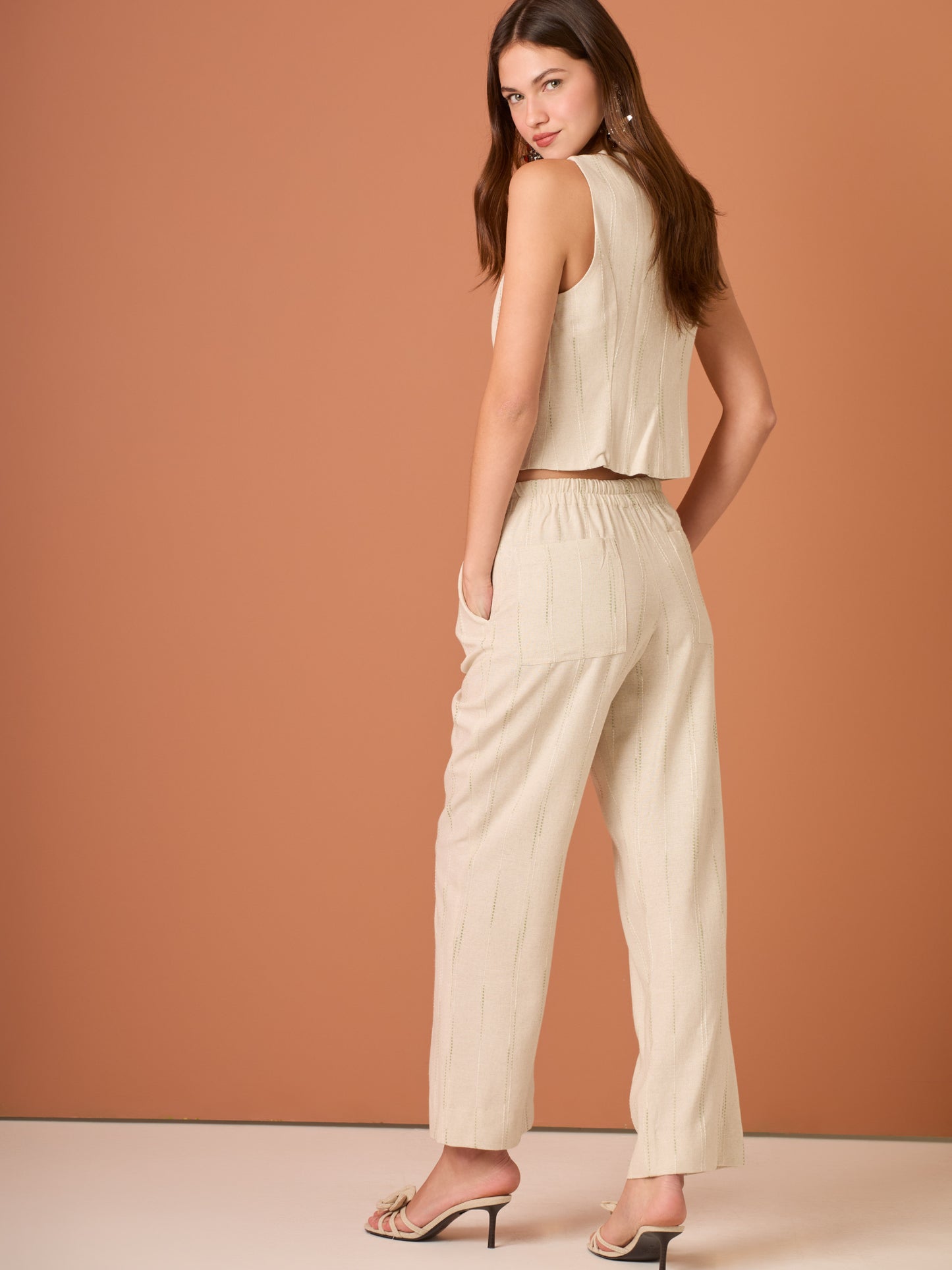 Blusa sin mangas de corte limpio y femenino. Cuello redondo y botonadura frontal con botones tipo joya; pinzas que definen el torso y bajo ligeramente curvado con pequeña abertura al centro. El sutil rayado vertical estiliza la figura. Ideal para combinar con el pantalón a juego o faldas altas para un look pulido.