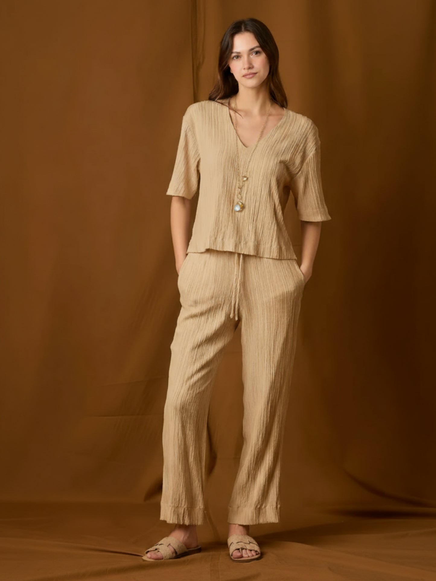 Pantalón fluido de silueta relajada y tiro medio, con pretina elástica y jareta ajustable. Pernera recta-amplia hasta el tobillo, bolsillos laterales y textura arrugada que aporta movimiento. Cómodo y versátil para el día a día o viajes; combínalo con tops mínima o la blusa a juego.