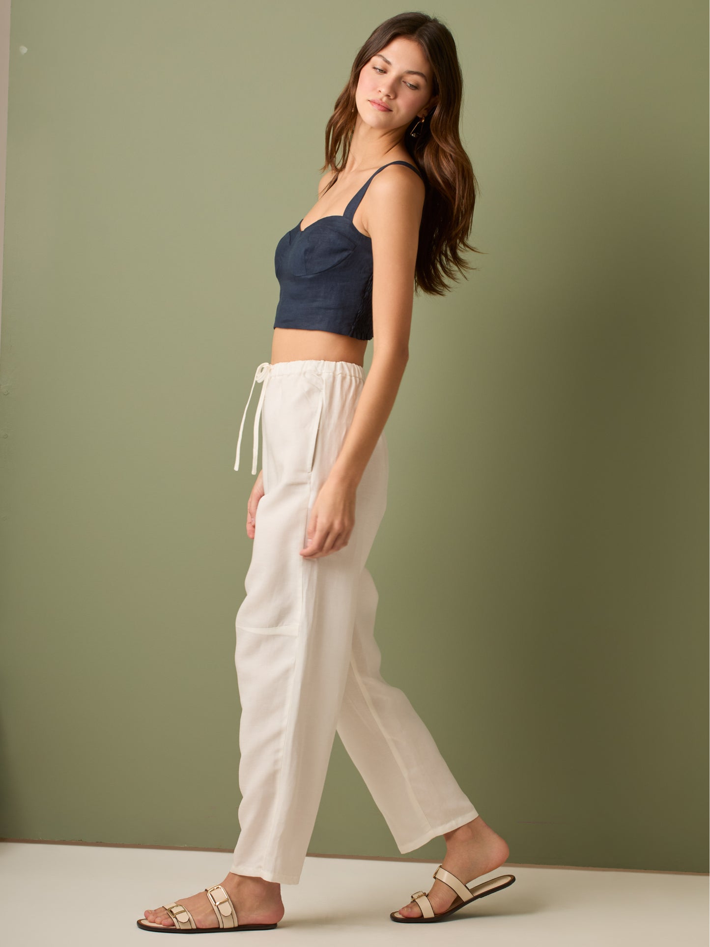 Pantalón de tiro medio con cintura elástica y cordón ajustable. Silueta relajada que cae con volumen en la cadera y se afina al tobillo, con bolsillos laterales y cortes decorativos en la pierna. Largo al tobillo con pequeña abertura en el bajo: la base moderna y versátil para elevar looks de día o de noche.