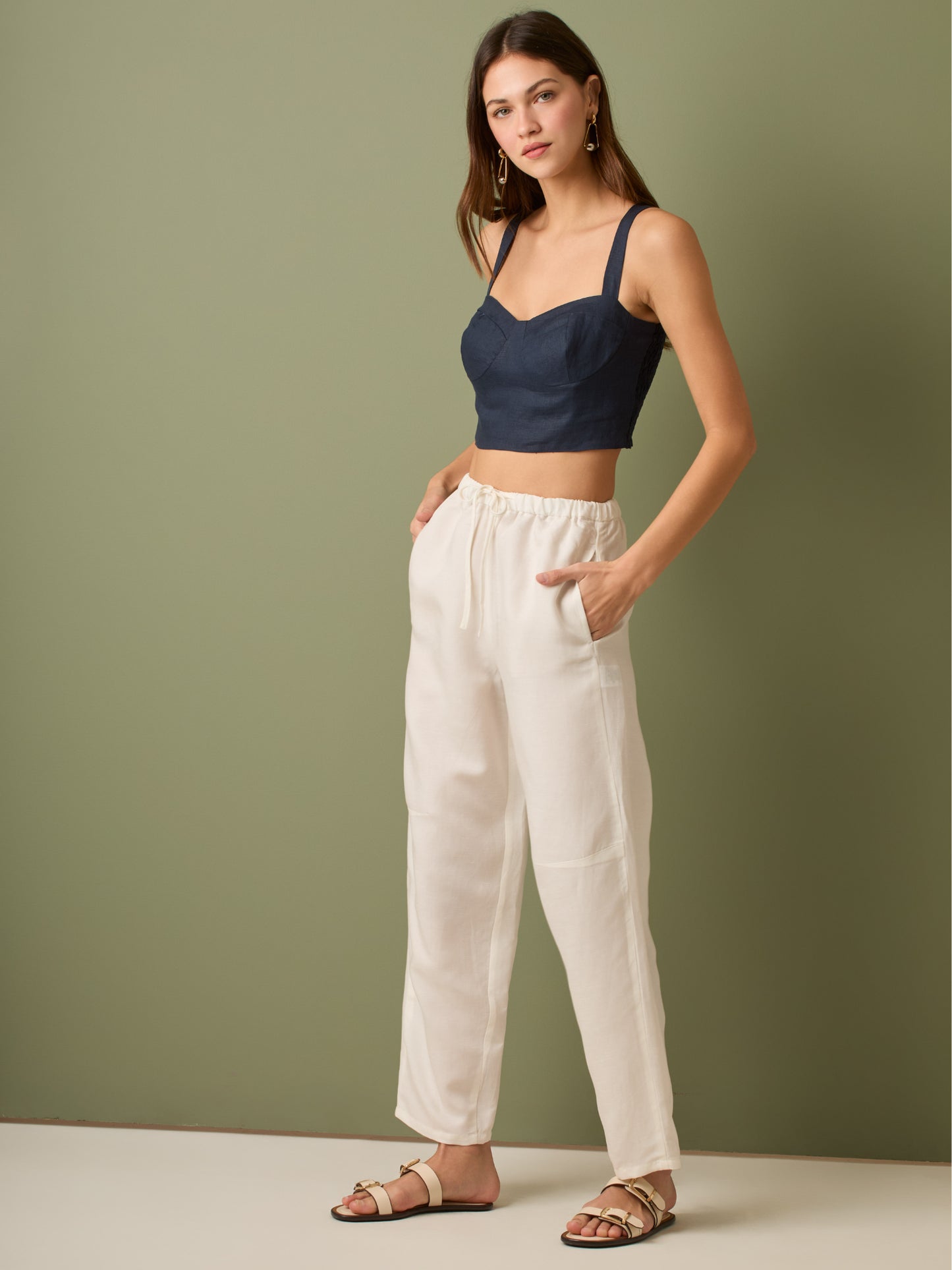 Pantalón de tiro medio con cintura elástica y cordón ajustable. Silueta relajada que cae con volumen en la cadera y se afina al tobillo, con bolsillos laterales y cortes decorativos en la pierna. Largo al tobillo con pequeña abertura en el bajo: la base moderna y versátil para elevar looks de día o de noche.