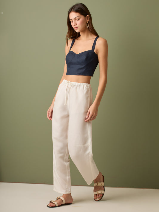 Pantalón de tiro medio con cintura elástica y cordón ajustable. Silueta relajada que cae con volumen en la cadera y se afina al tobillo, con bolsillos laterales y cortes decorativos en la pierna. Largo al tobillo con pequeña abertura en el bajo: la base moderna y versátil para elevar looks de día o de noche.