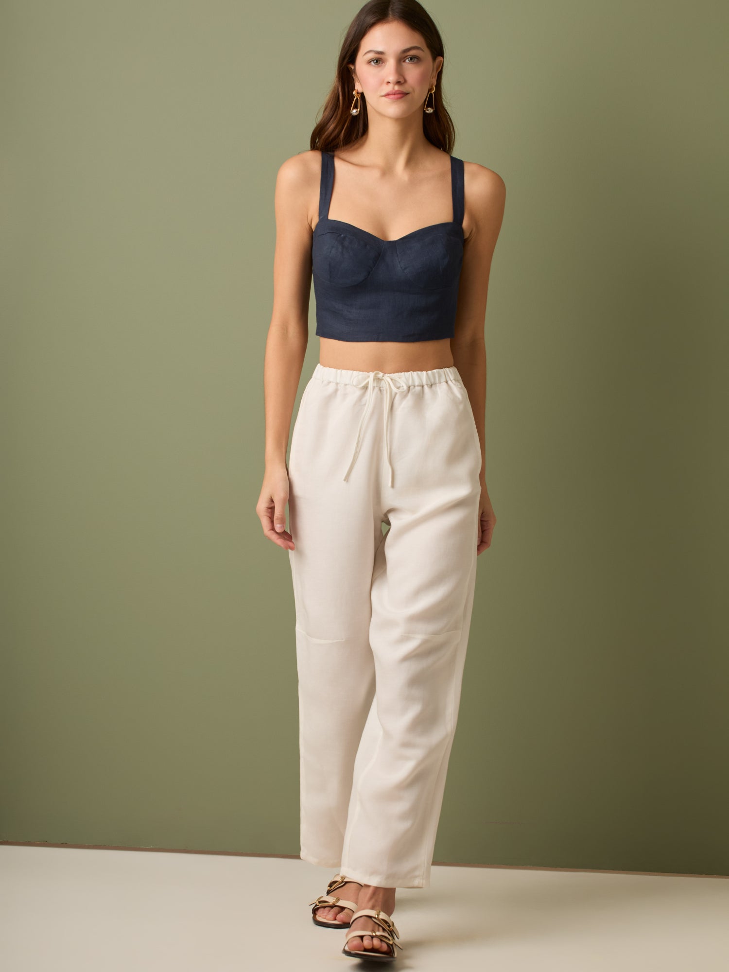 Pantalón de tiro medio con cintura elástica y cordón ajustable. Silueta relajada que cae con volumen en la cadera y se afina al tobillo, con bolsillos laterales y cortes decorativos en la pierna. Largo al tobillo con pequeña abertura en el bajo: la base moderna y versátil para elevar looks de día o de noche.