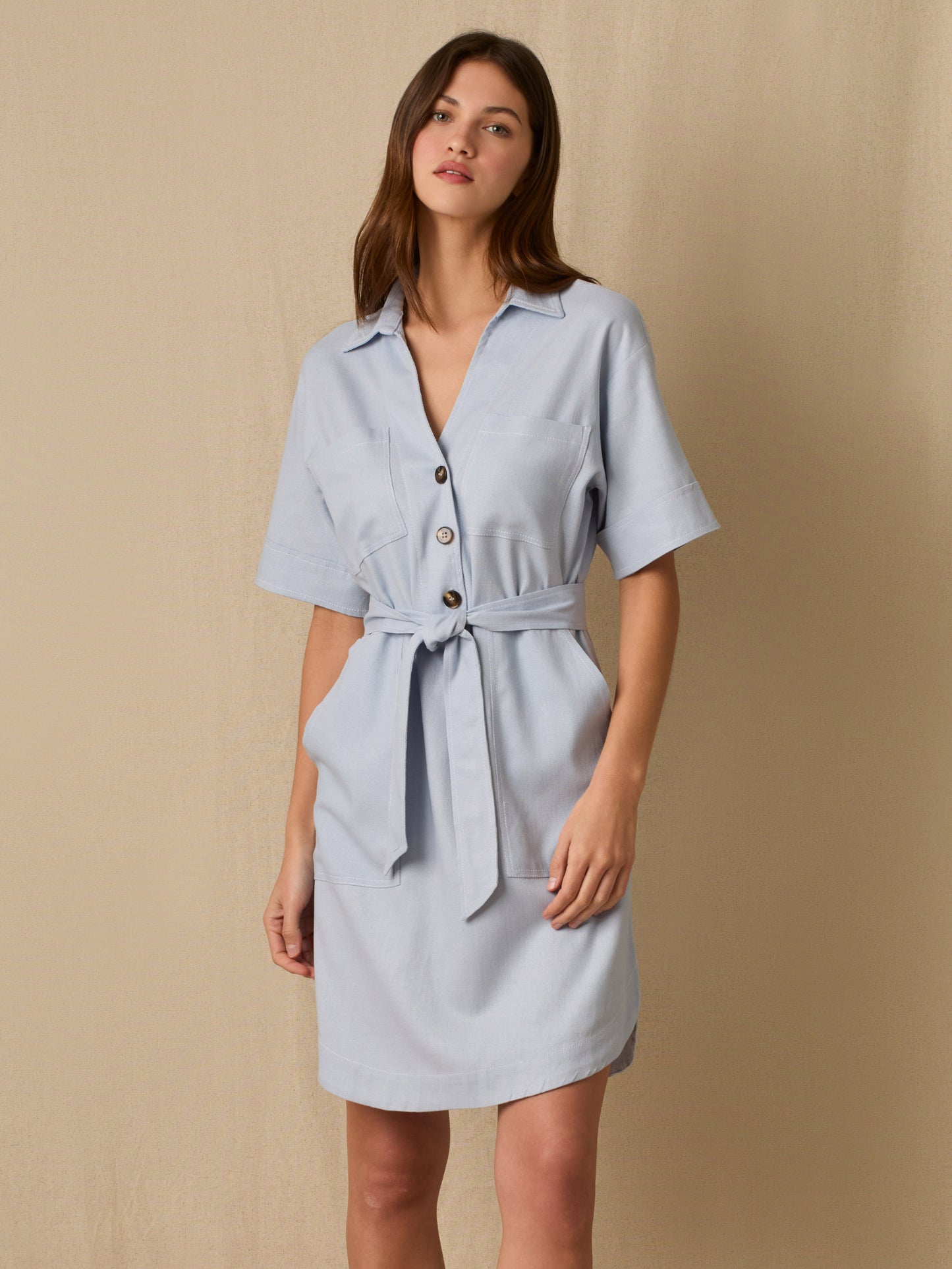 Este vestido camisero de silueta recta combina la estructura de una prenda utilitaria con la frescura de un look contemporáneo. Con cuello tipo solapa, botones frontales contrastantes y bolsillos superiores de parche, incorpora un cinturón del mismo tejido que define la cintura y aporta feminidad. El largo sobre la rodilla lo convierte en una opción versátil para días cálidos, perfecta para el trabajo, una salida casual o un look urbano pulido.