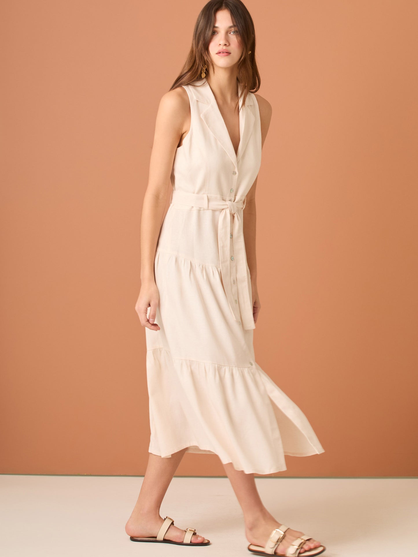 Vestido midi sin mangas con solapa tipo sastre, botonadura frontal y corte en la cintura que se ajusta con lazo, terminado en falda con volantes amplios