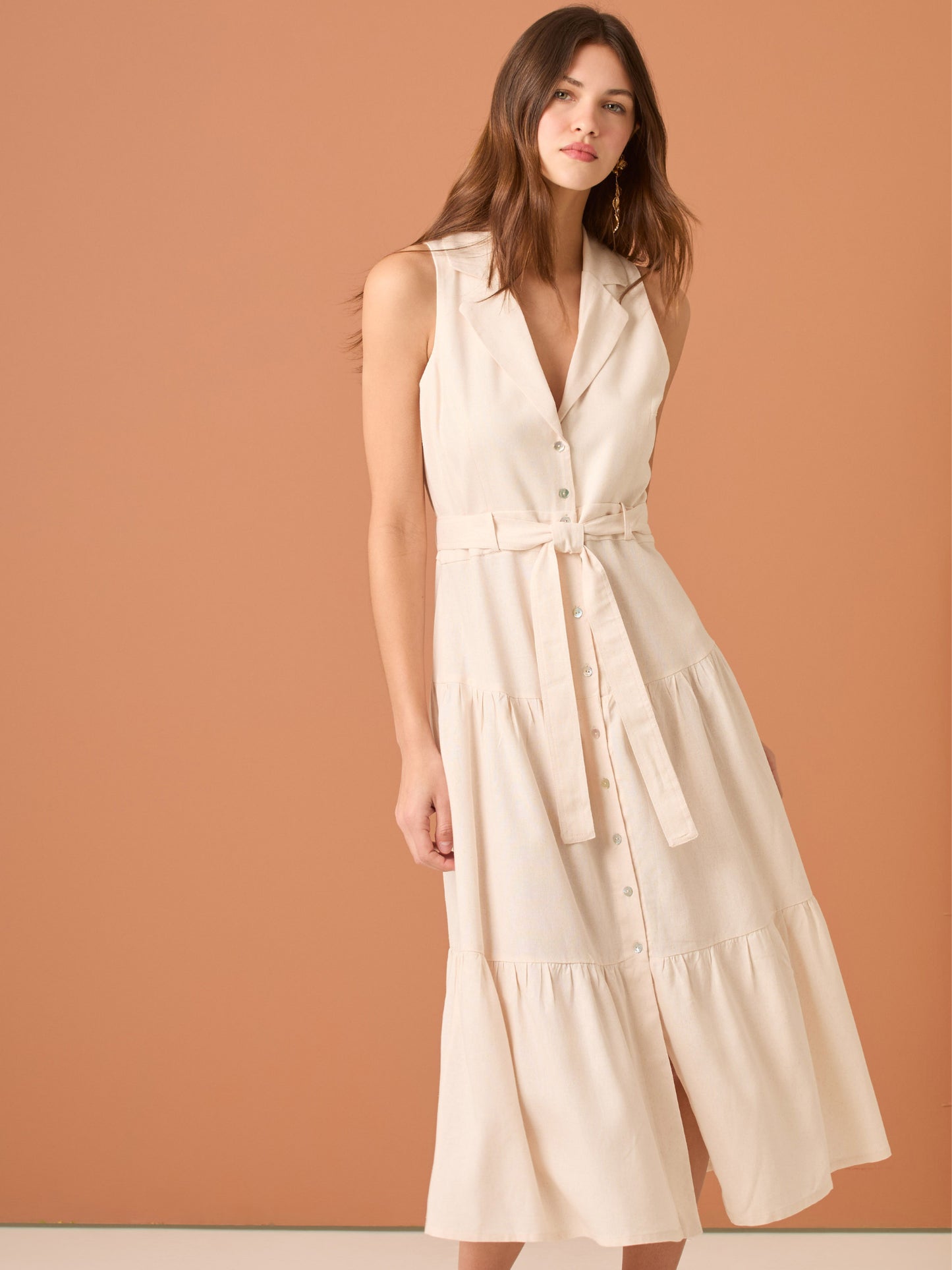 Vestido midi sin mangas con solapa tipo sastre, botonadura frontal y corte en la cintura que se ajusta con lazo, terminado en falda con volantes amplios