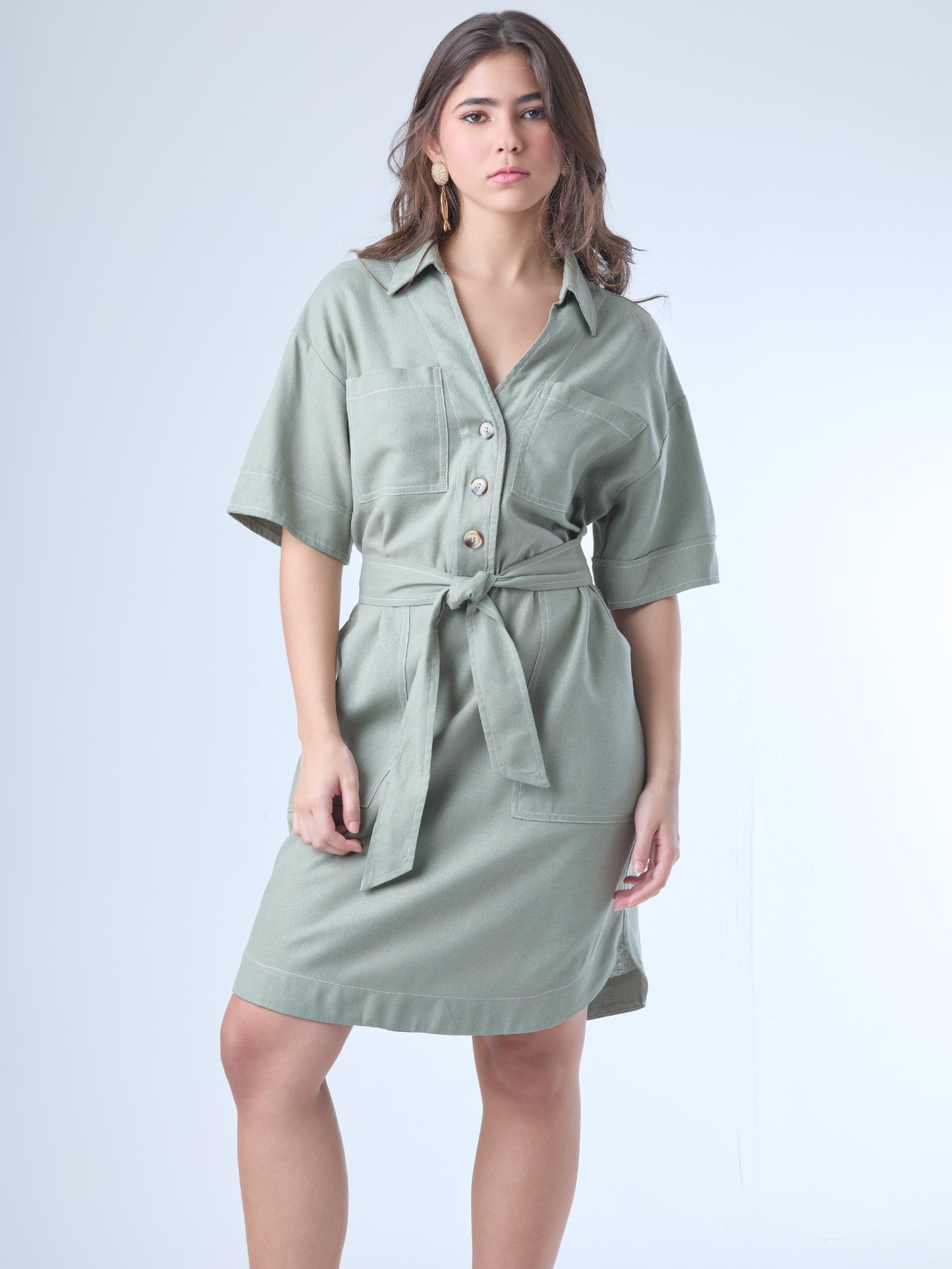 Este vestido camisero de silueta recta combina la estructura de una prenda utilitaria con la frescura de un look contemporáneo. Con cuello tipo solapa, botones frontales contrastantes y bolsillos superiores de parche, incorpora un cinturón del mismo tejido que define la cintura y aporta feminidad. El largo sobre la rodilla lo convierte en una opción versátil para días cálidos, perfecta para el trabajo, una salida casual o un look urbano pulido.