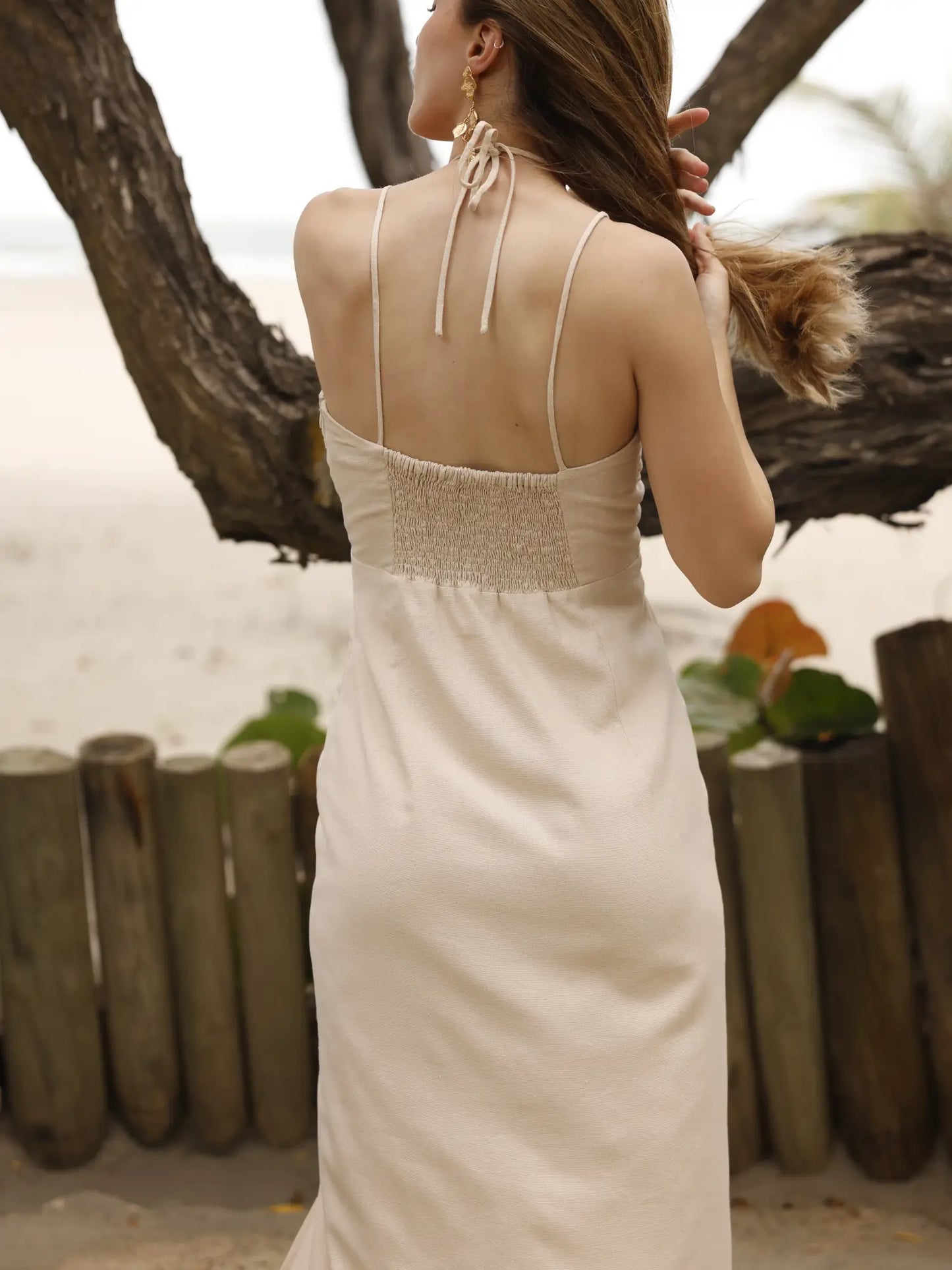 Vestido largo de tirantes delgados con escote halter. Tiene un detalle fruncido en el busto con abertura frontal y un pequeño corte debajo del pecho. La falda incluye una abertura frontal que aporta movimiento y frescura al diseño. Silueta ajustada al cuerpo con caída fluida. Ideal para un look de playa o verano.