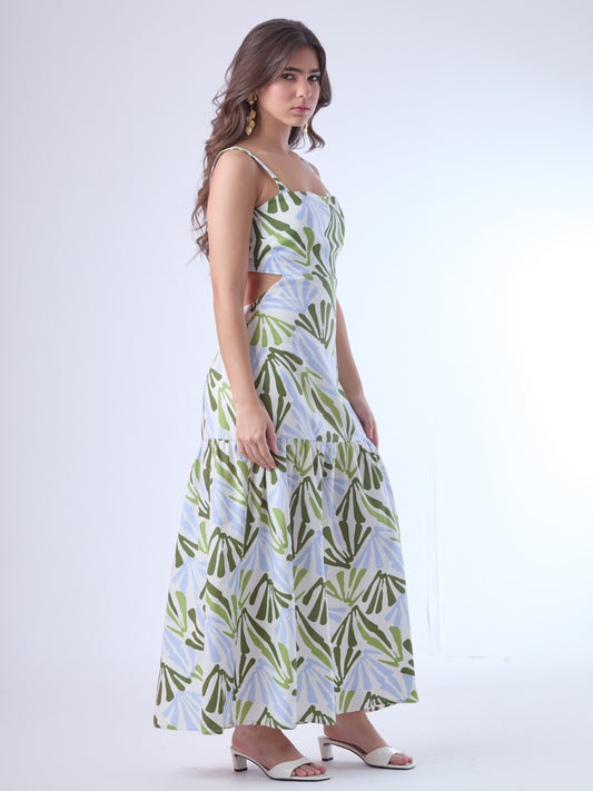 Este vestido largo presenta un diseño fresco y moderno con estampado botánico en tonos verde oliva, verde lima y azul claro sobre fondo blanco. Tiene tirantes anchos y escote recto, que aportan estructura y realzan los hombros. Los laterales descubiertos le dan un toque contemporáneo y femenino, acentuando la figura de forma sutil. La falda cae en línea recta con un corte bajo y un ligero fruncido, lo que aporta movimiento y una silueta relajada. Es una prenda ideal para climas cálidos y ocasiones casuales