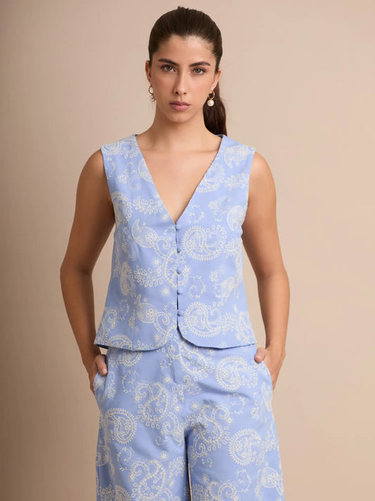 La blusa Chela Baby Blue destaca por su escote en V profundo y su botonadura frontal que aporta un toque sastrero y elegante. Su estampado suave estilo paisley y corte estructurado la convierten en una pieza ideal para elevar cualquier look de día.