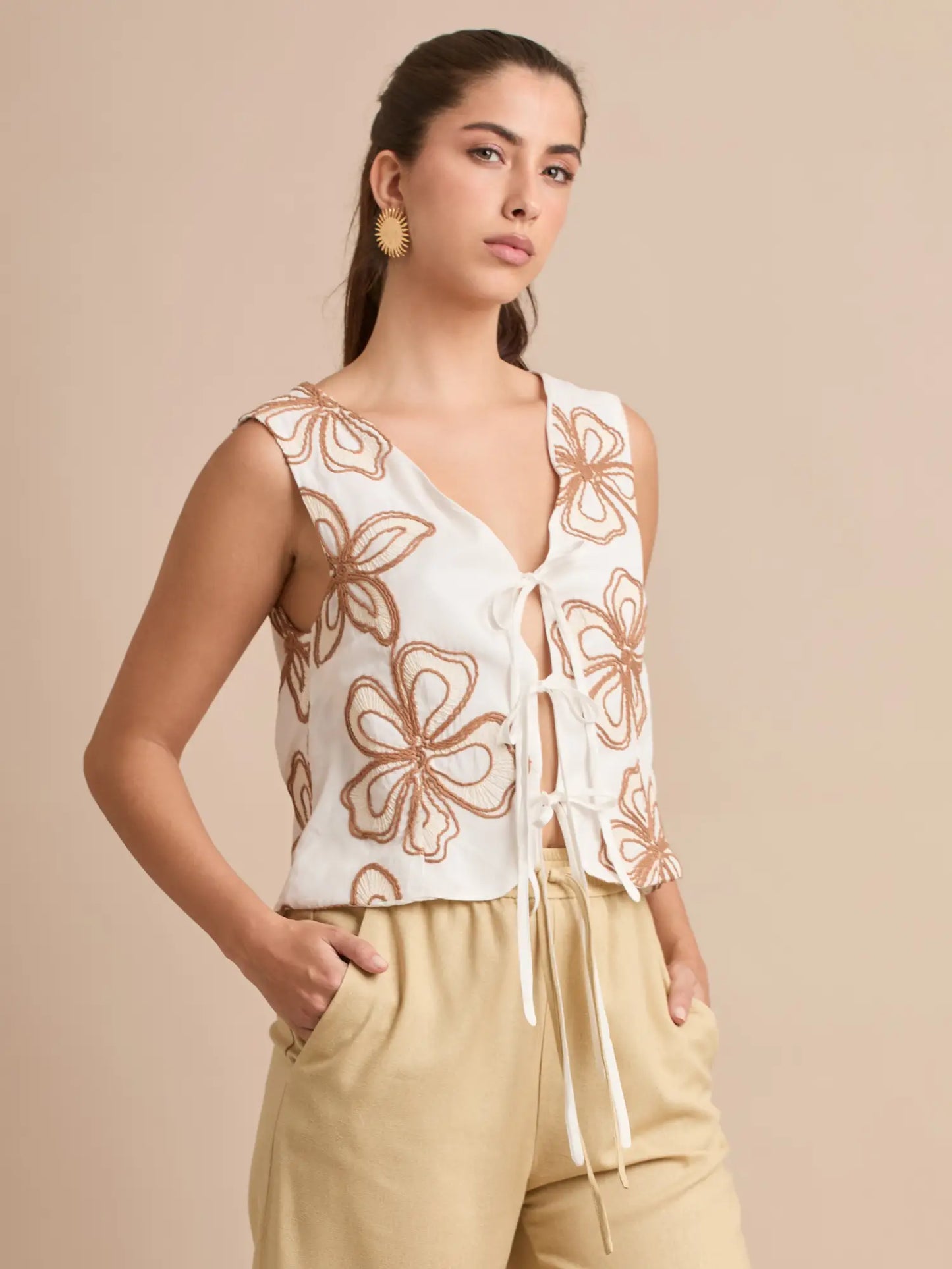 La blusa Corfú blanca destaca por su bordado floral en tonos café y su cierre con lazos, creando un diseño femenino, fresco y perfecto para looks veraniegos y naturales.
