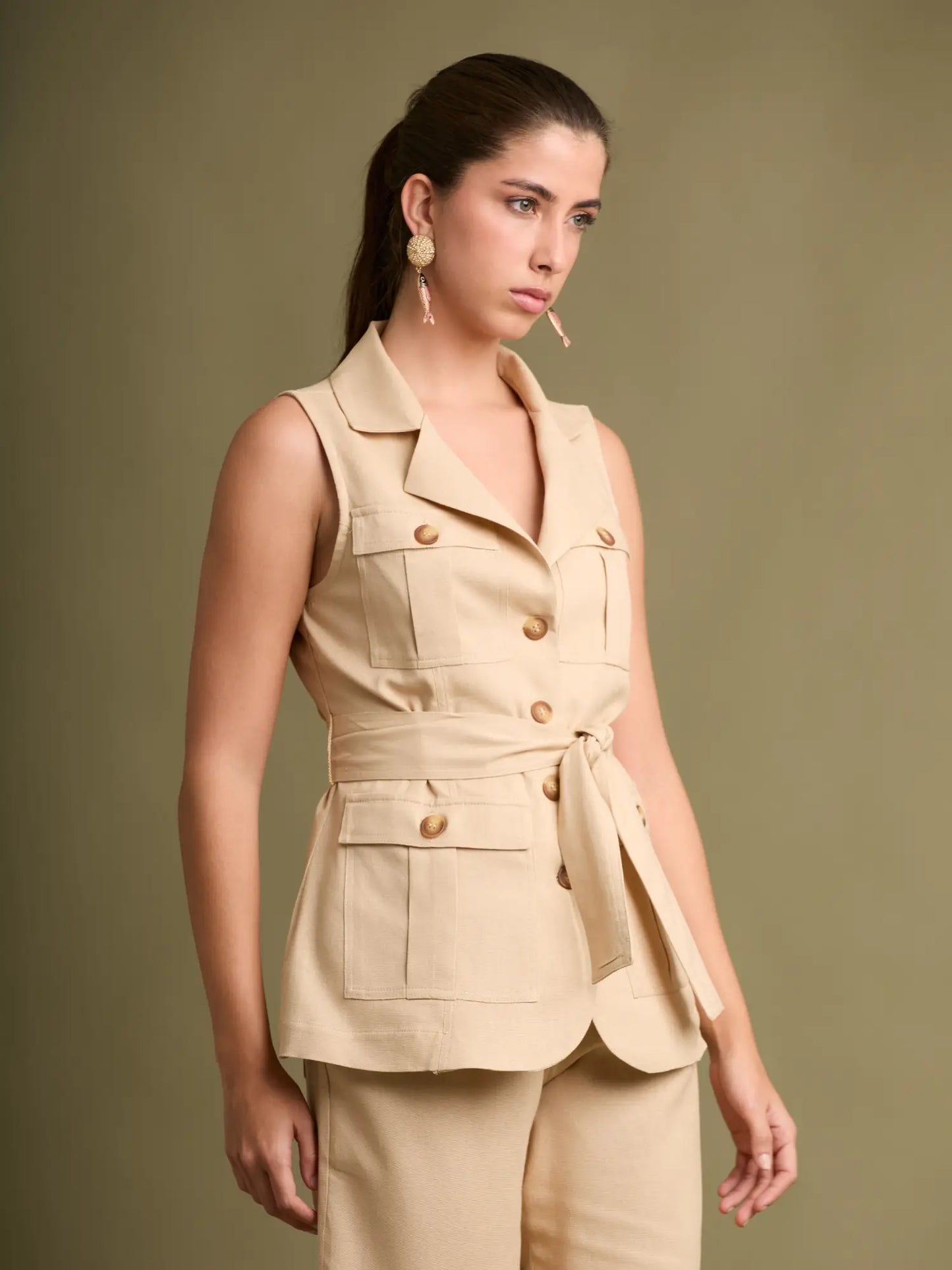 La blusa tipo chaleco beige combina estilo y funcionalidad con sus cuatro bolsillos frontales, botonadura clásica y un cinturón que realza la figura con sutileza.