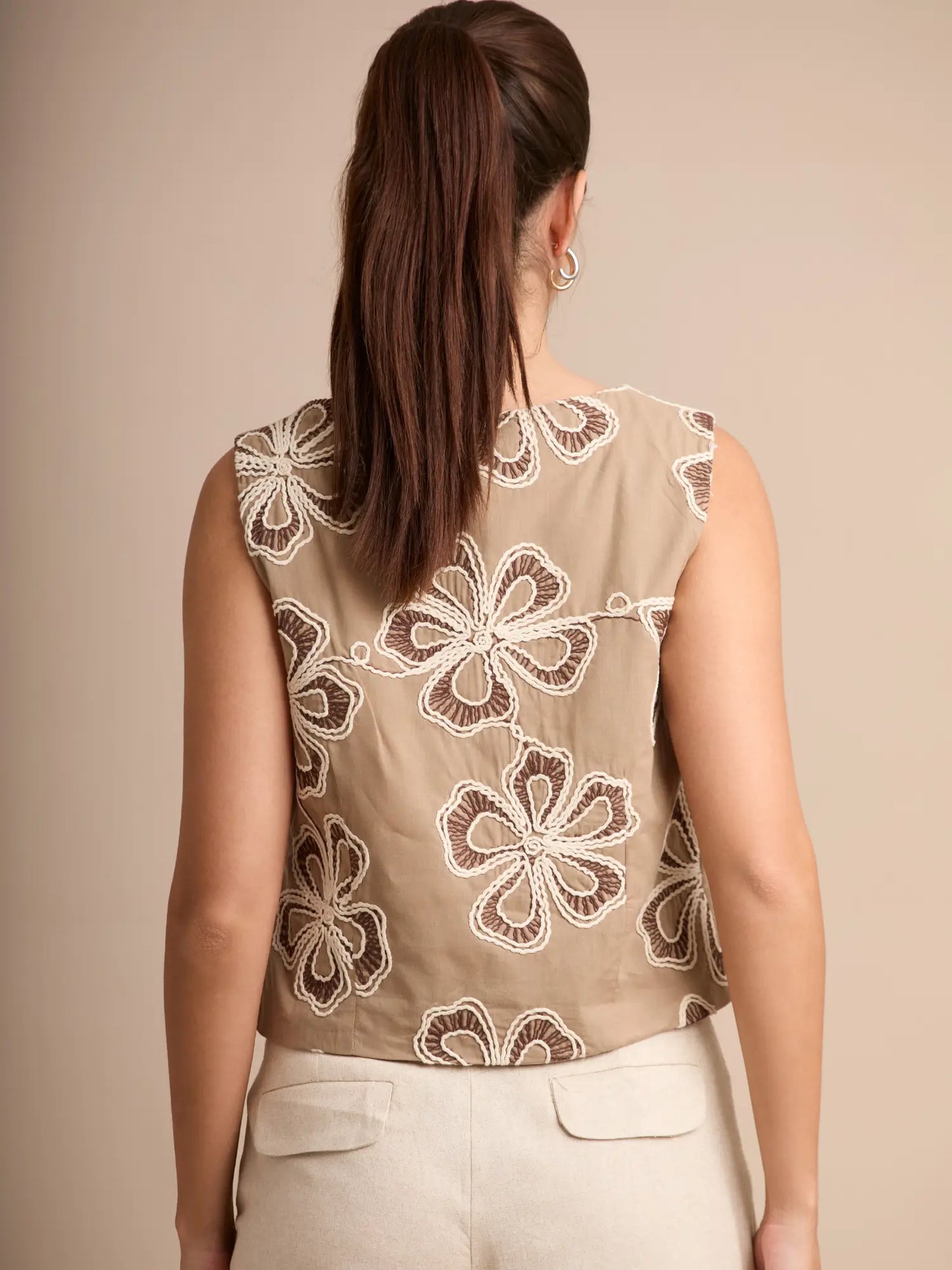 Este chaleco beige boho presenta una abertura frontal ajustada con lazos y un bordado artesanal en tonos crema, creando una pieza única y elegante para cualquier temporada.