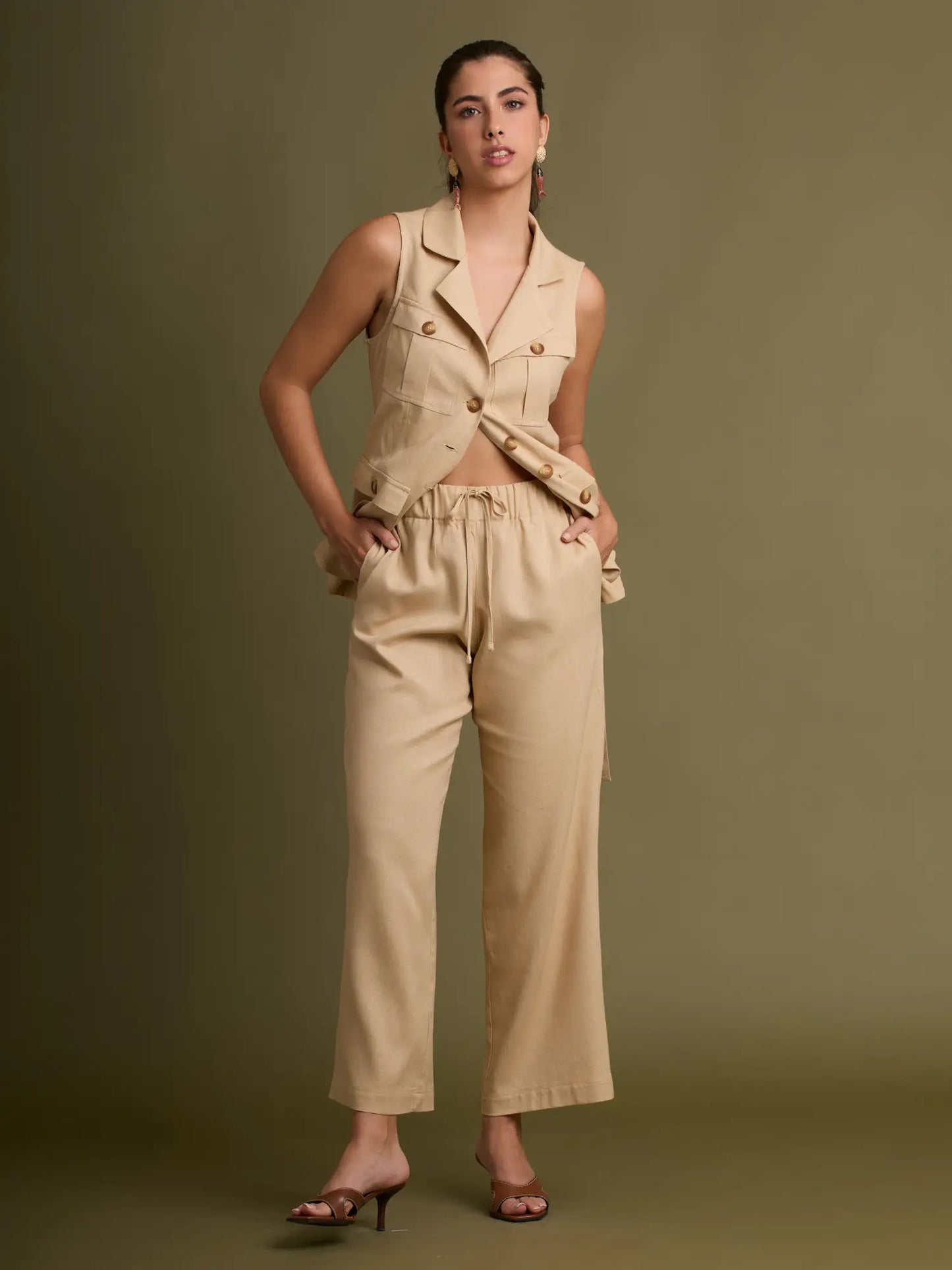 La blusa sin mangas beige presenta cuello solapa, bolsillos funcionales y una textura suave que la hace perfecta para combinar con pantalones o shorts del mismo tono.