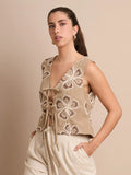 El chaleco Corfú beige destaca por su bordado floral artesanal y sus lazos frontales, que crean un look femenino, fresco y fácil de combinar con tonos neutros o tierra.