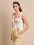 El chaleco Corfú boho presenta una abertura frontal atada con lazos y un hermoso bordado floral que lo convierte en una prenda clave para un estilo relajado y veraniego.