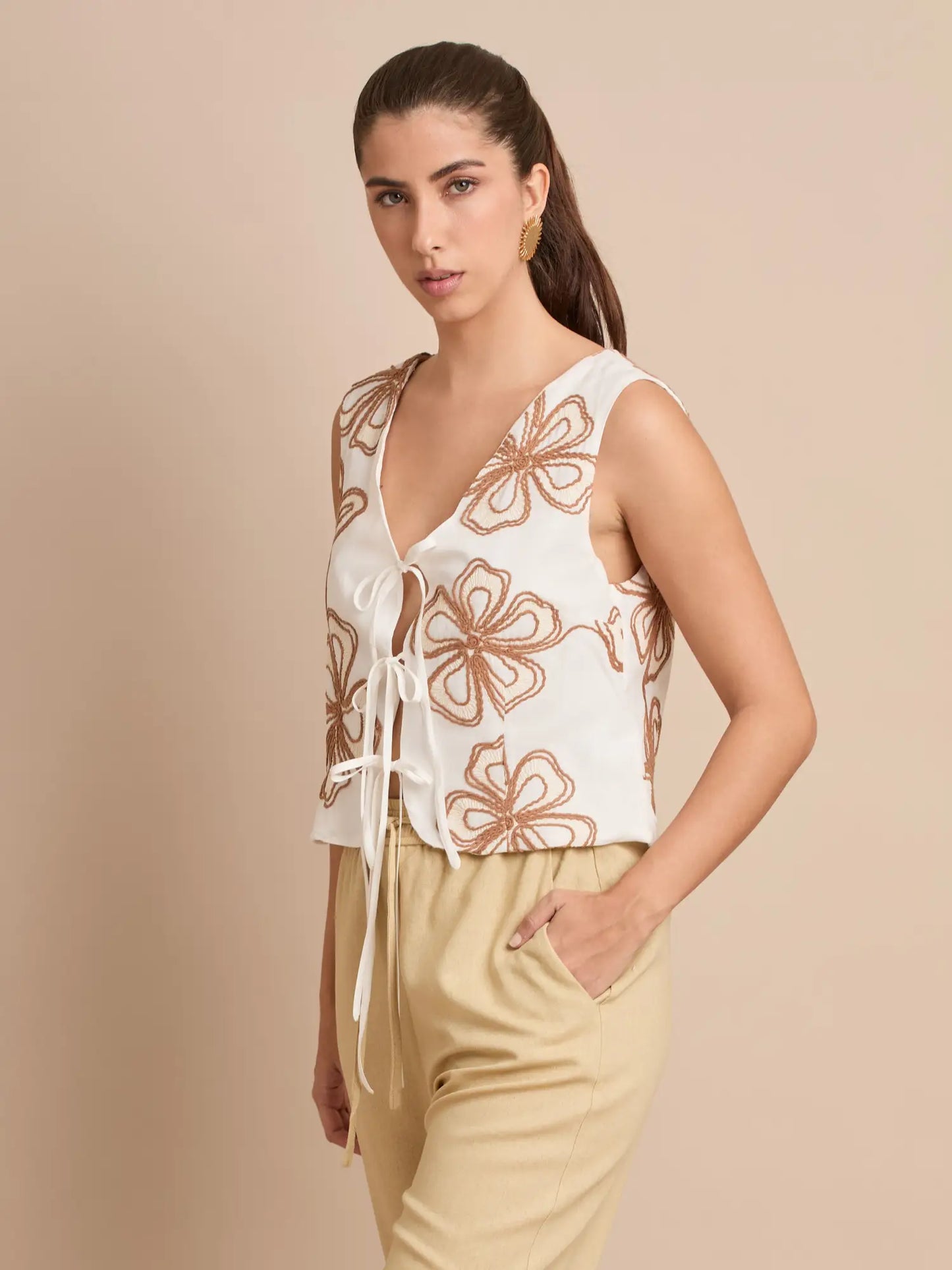 El chaleco Corfú boho presenta una abertura frontal atada con lazos y un hermoso bordado floral que lo convierte en una prenda clave para un estilo relajado y veraniego.