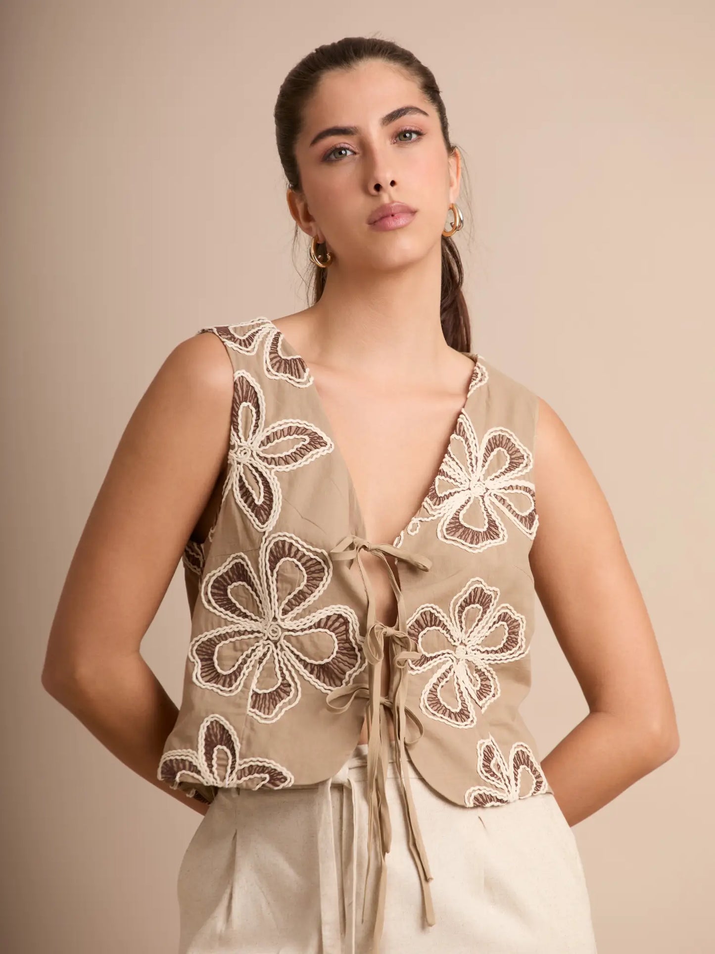 El chaleco color arena combina bordados florales en contraste y lazos ajustables que aportan ligereza y movimiento. Perfecto para looks relajados y veraniegos.