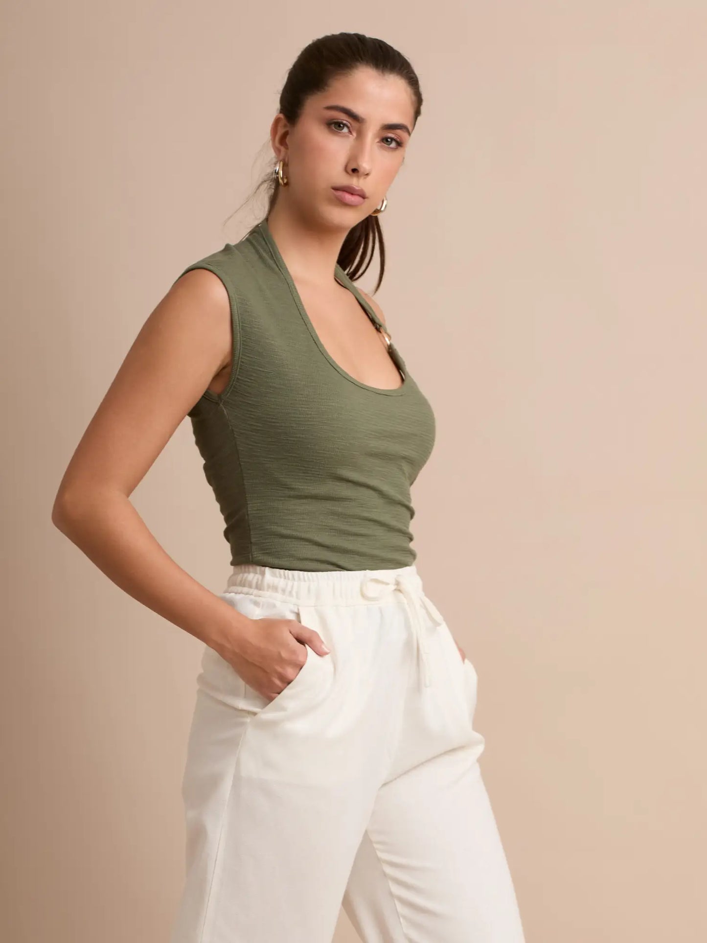 Confeccionado en un tejido suave y adaptable, este top verde olivo destaca por su tirante halter con un aro dorado que enmarca el escote. Una opción moderna que complementa a la perfección looks relajados o chic.