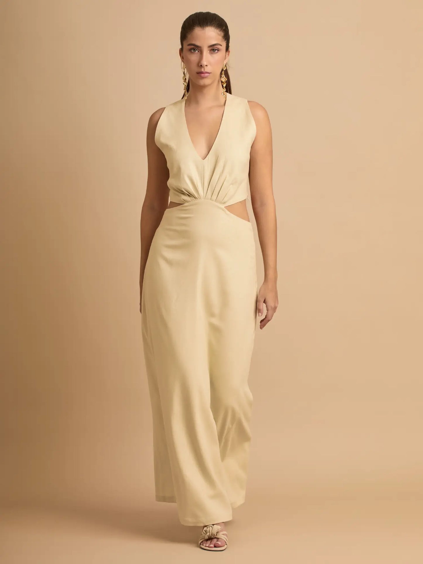 El vestido beige combina un escote profundo en V con cut-outs laterales que estilizan la cintura. Su diseño elegante y moderno es ideal para eventos, cenas o looks de verano sofisticados.