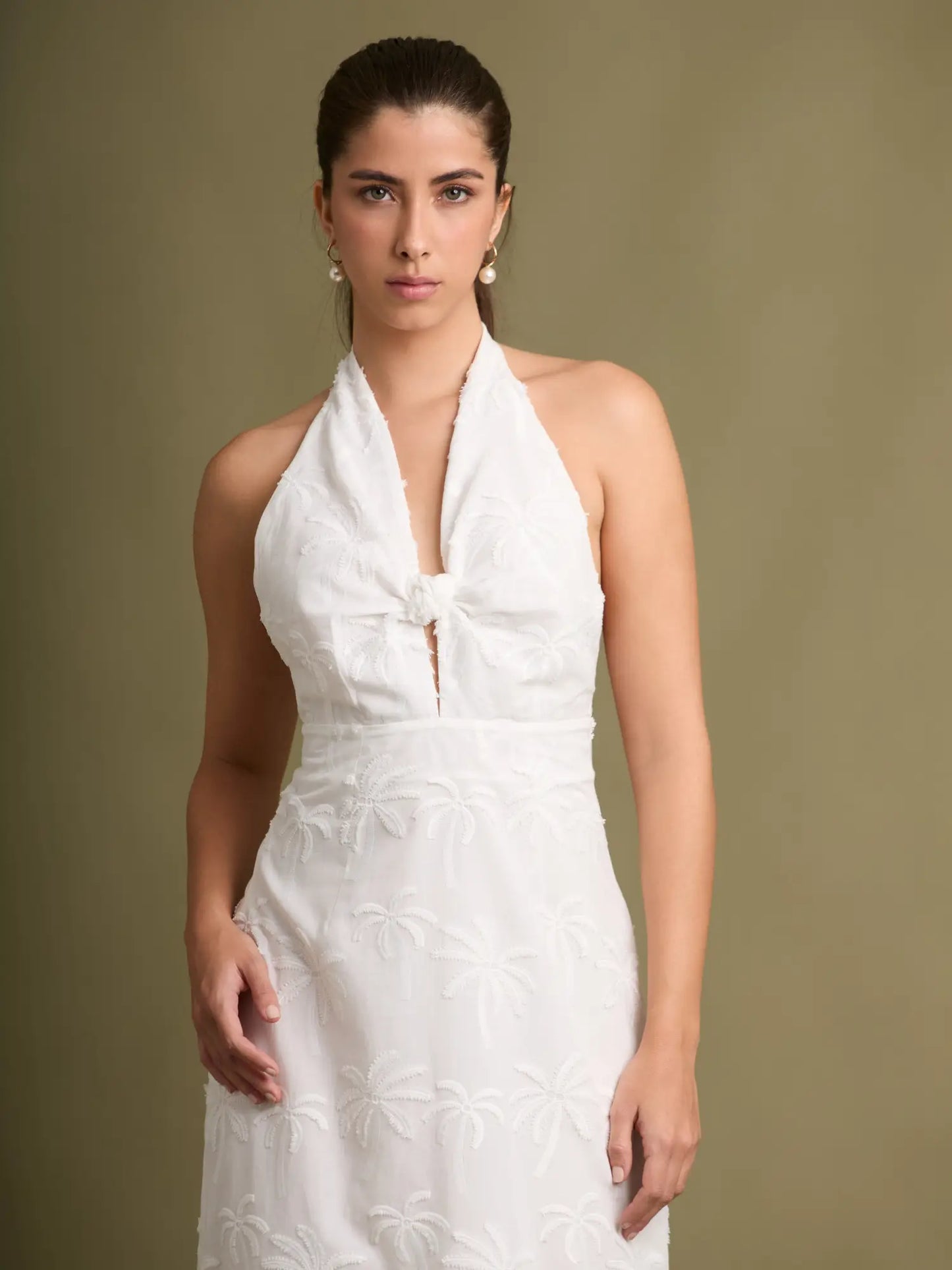 Una pieza femenina y elegante con textura bordada inspirada en palmeras. Su escote halter con nudo y silueta recta crean un look estilizado y atemporal.