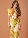 Vestido largo con estampado tropical en tonos cálidos, tiene mangas cortas, un diseño de nudo en la cintura que resalta la figura, y está confeccionado en una tela ligera, ideal para climas cálidos o eventos casuales.